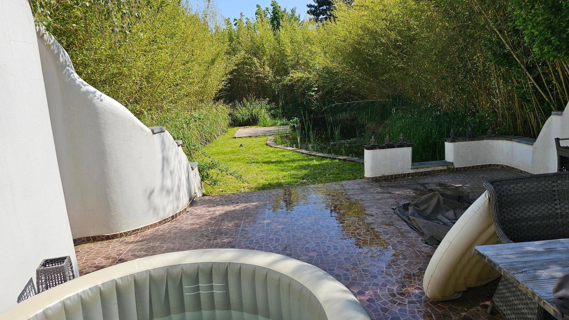 Gepflasterte Terrasse mit Whirlpool und Blick auf den grünen Garten mit Teich und Bambus.