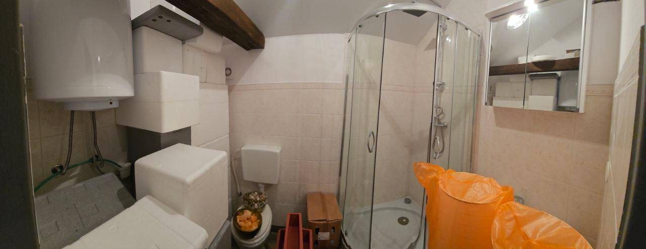 Badezimmer mit Duschkabine, Warmwasserboiler und Fliesen an Wänden und Boden.