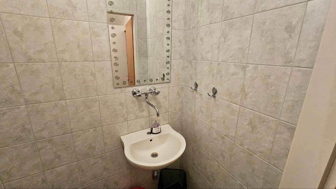Kleines Gäste-WC mit Waschbecken, Spiegel und hellen Wandfliesen.
