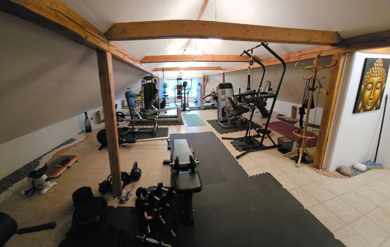 Geräumiger Fitnessraum im Dachgeschoss mit sichtbaren Holzbalken, Schrägdach und verschiedenen Trainingsgeräten.