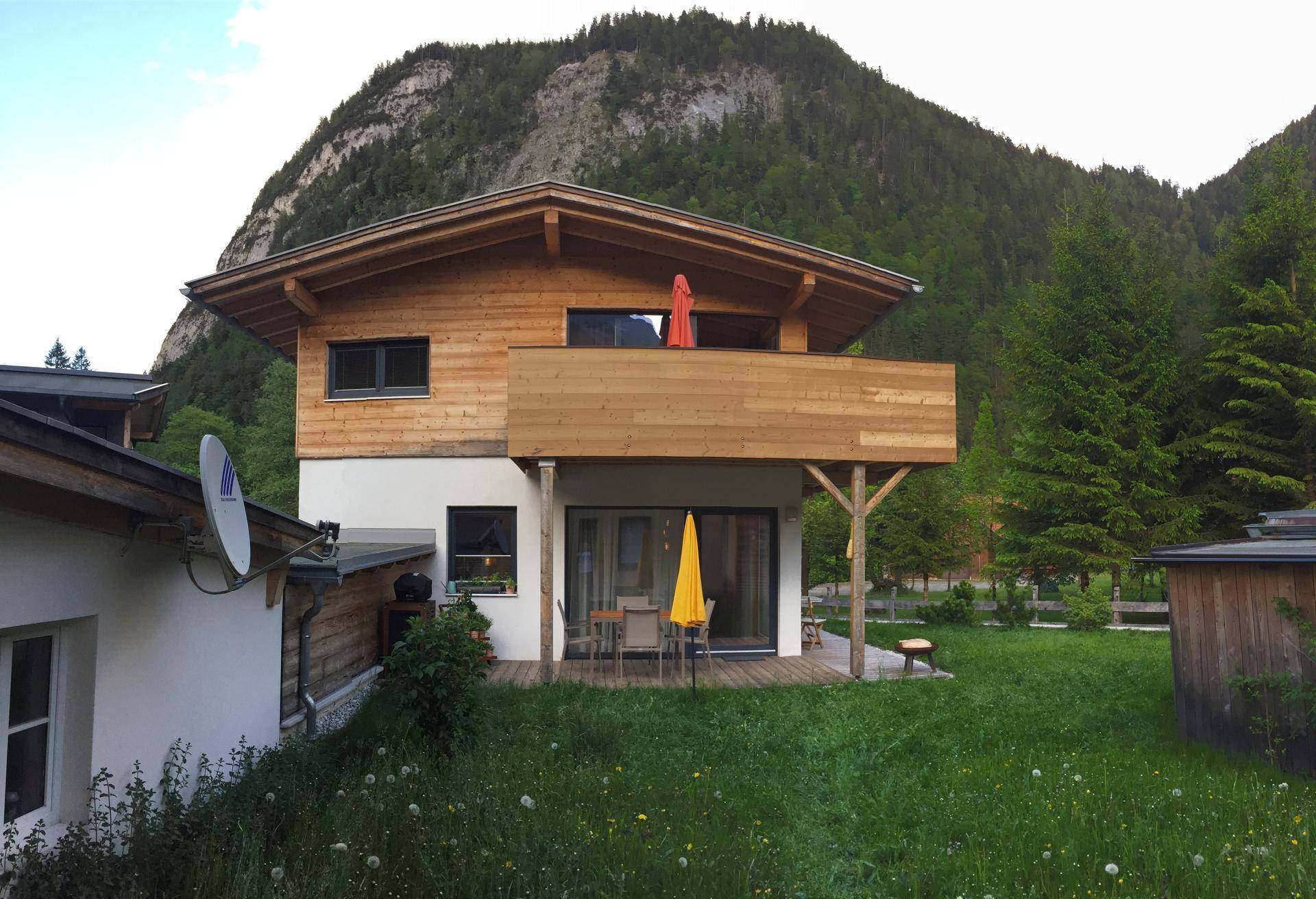 Freistehendes Chalet mit Garten, Terrasse und Balkon vor alpiner Bergkulisse.