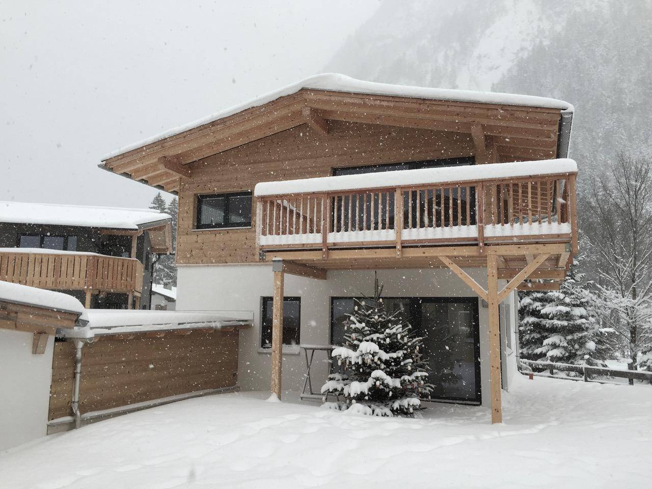 Chalet im Winter mit verschneitem Garten, Holzbalkon und Tannenbaum.