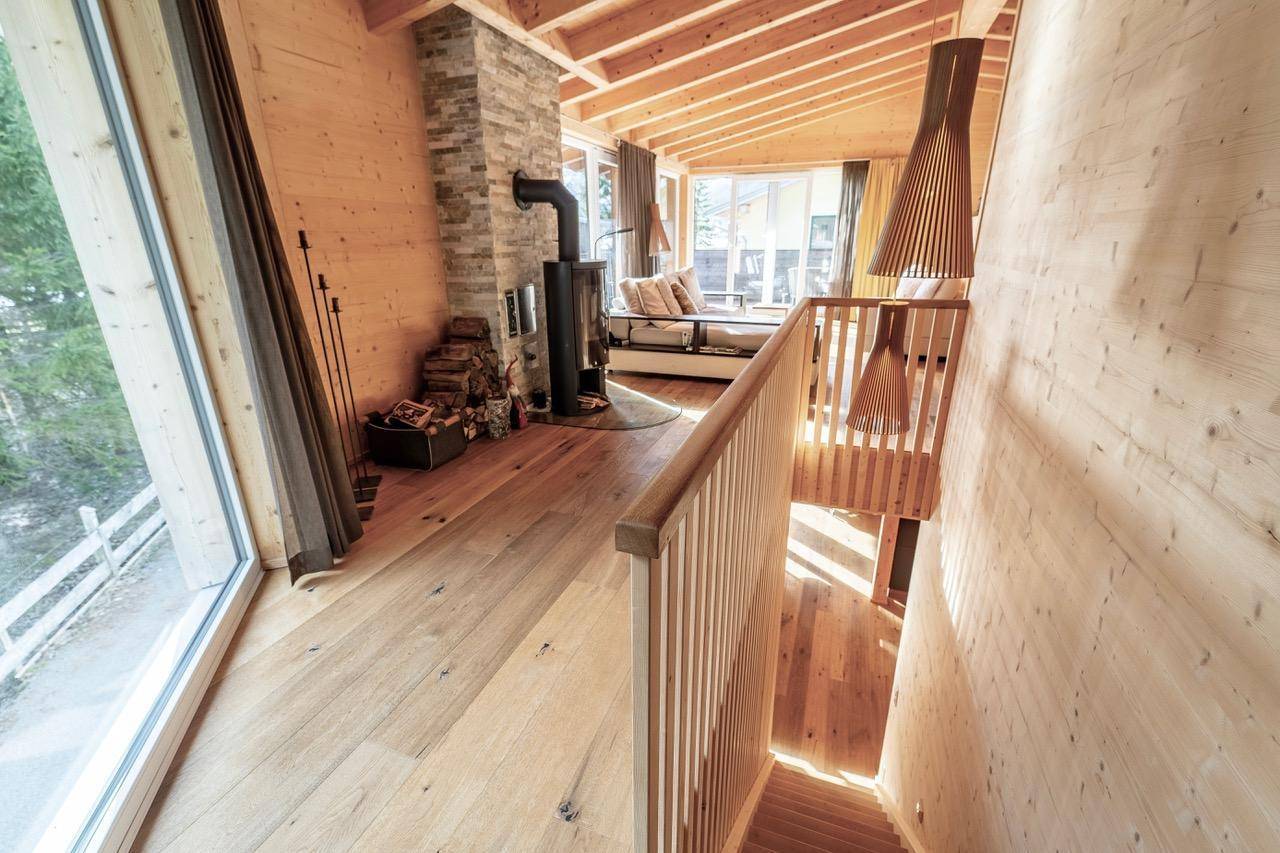 Heller Flur mit Holztreppe und Blick in den offenen Wohnbereich mit Kamin.