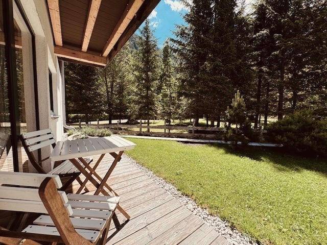 Sonniger Terrassenbereich mit Holzboden, Gartenmöbeln und Blick ins Grüne.
