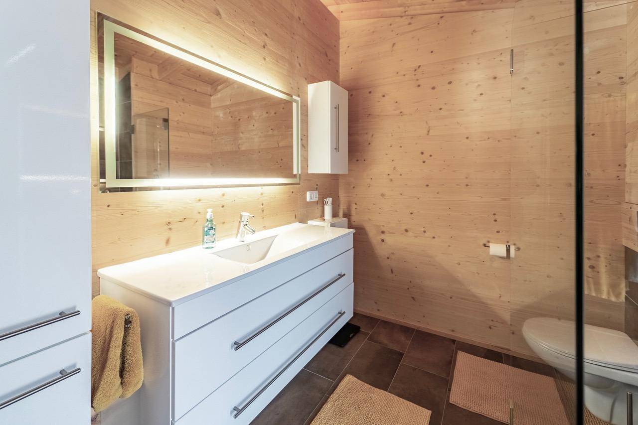 Modernes Badezimmer mit Holzvertäfelung, beleuchtetem Spiegel und Waschtisch.