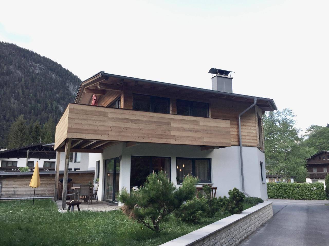 Modernes Chalet mit Holzbalkon, weißer Fassade und Bergblick.