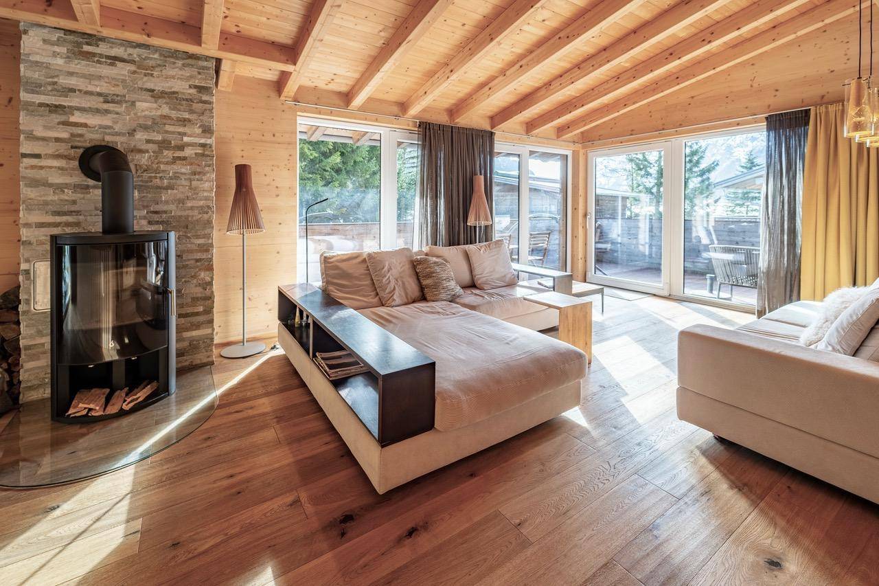 Lichtdurchflutetes Wohnzimmer mit Kamin, bequemer Couch und großen Fensterfronten.