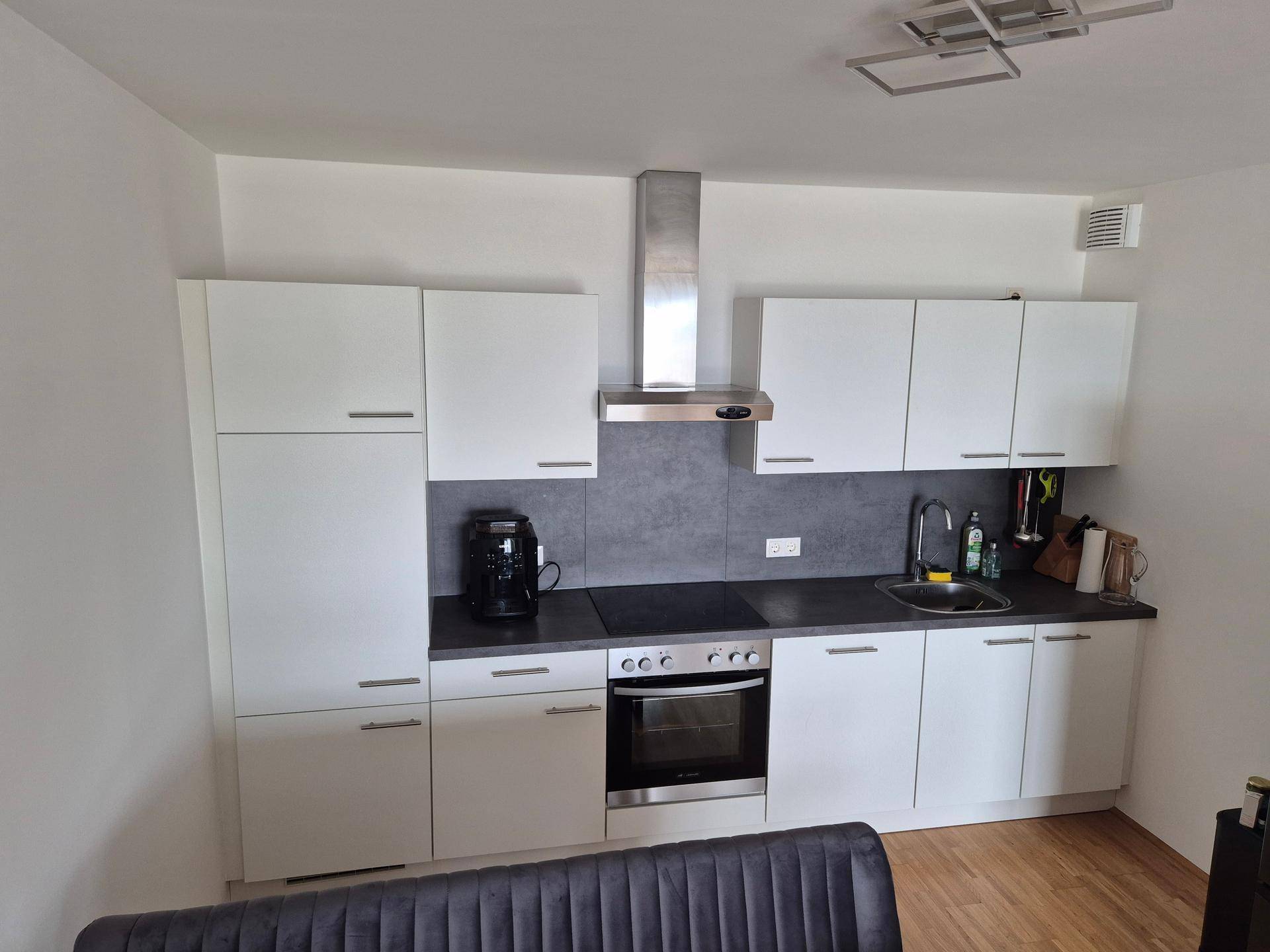 Moderne Einbauküche mit weißen Schränken, dunkler Arbeitsplatte und integrierten Geräten, funktional und stilvoll.