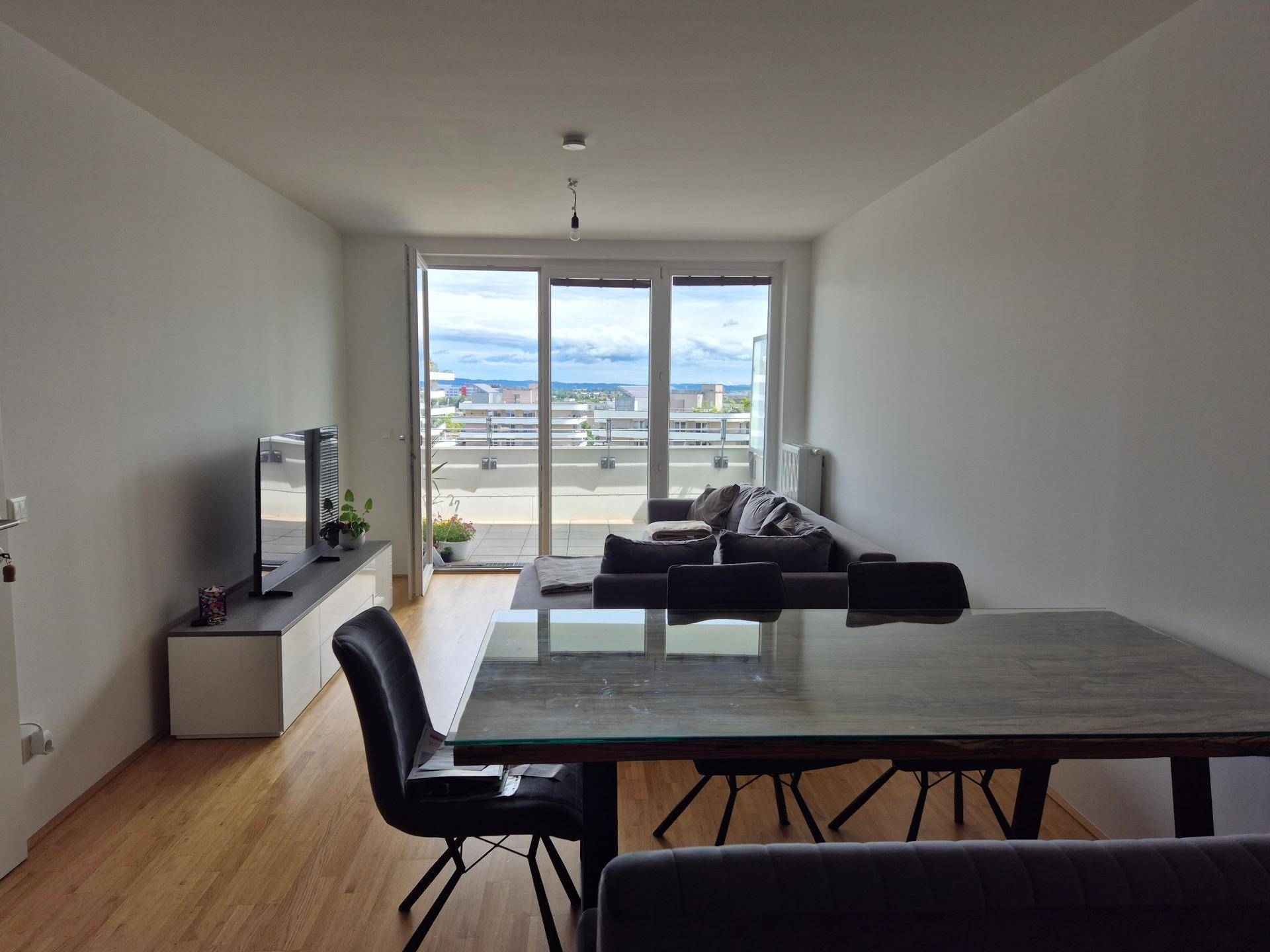 Heller Wohn-Essbereich mit modernem Esstisch und Zugang zum Balkon, der einen weiten Blick bietet.