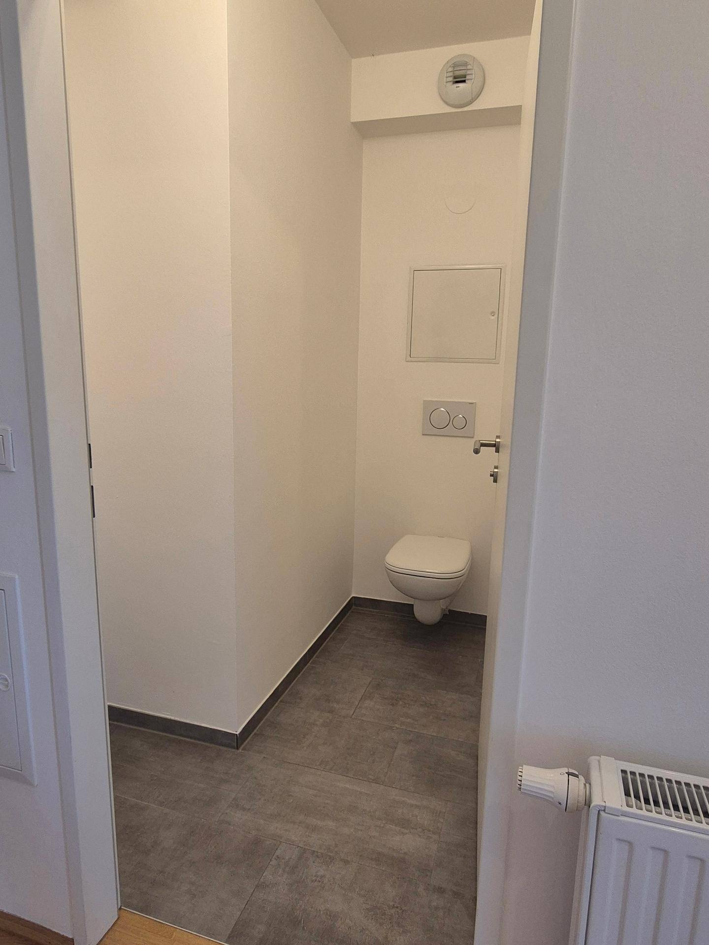 Kleines Gäste-WC mit wandhängender Toilette und modernen grauen Fliesen auf dem Boden.