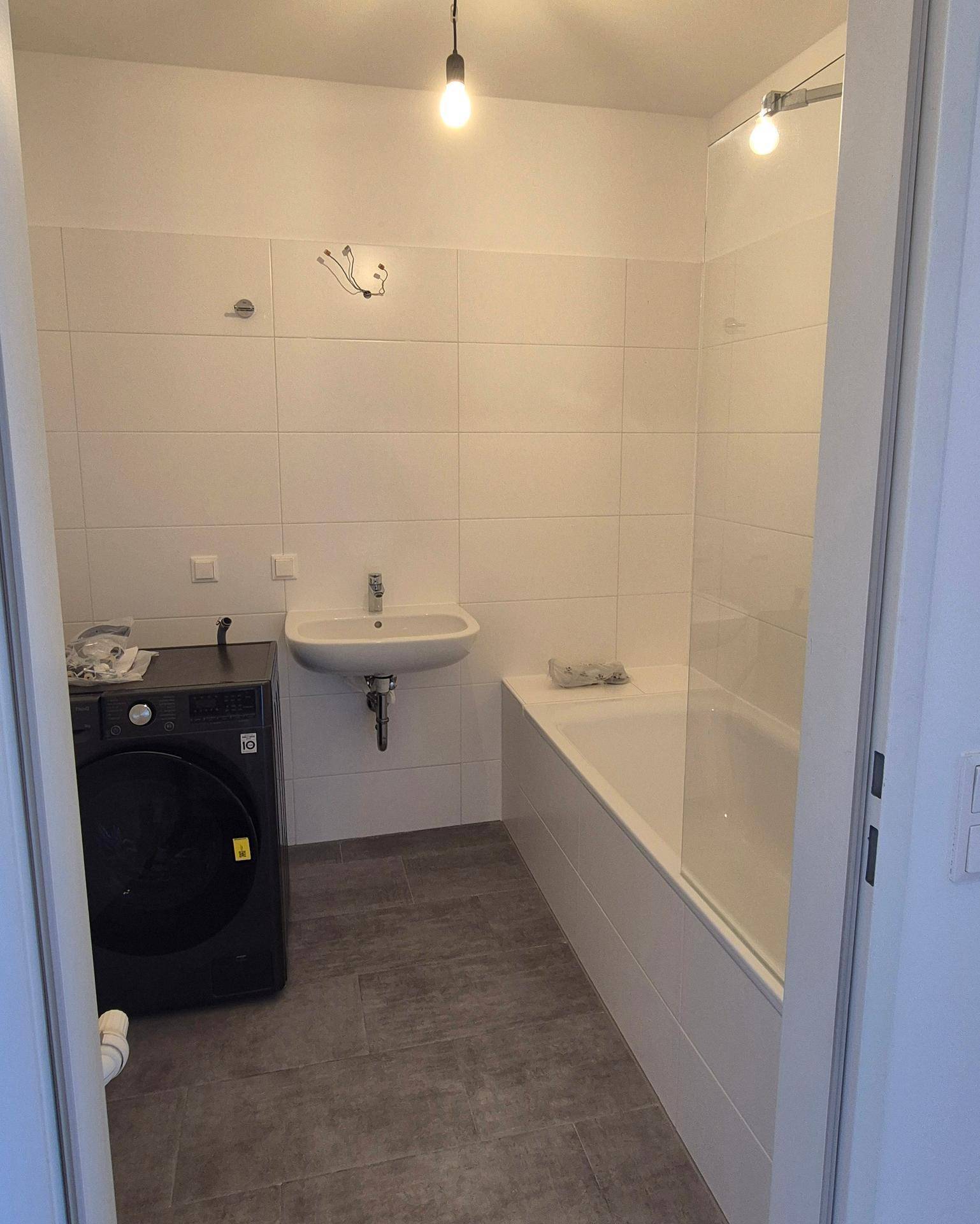 Modernes Badezimmer mit Badewanne, Waschmaschine, Waschbecken und hellen Wandfliesen.
