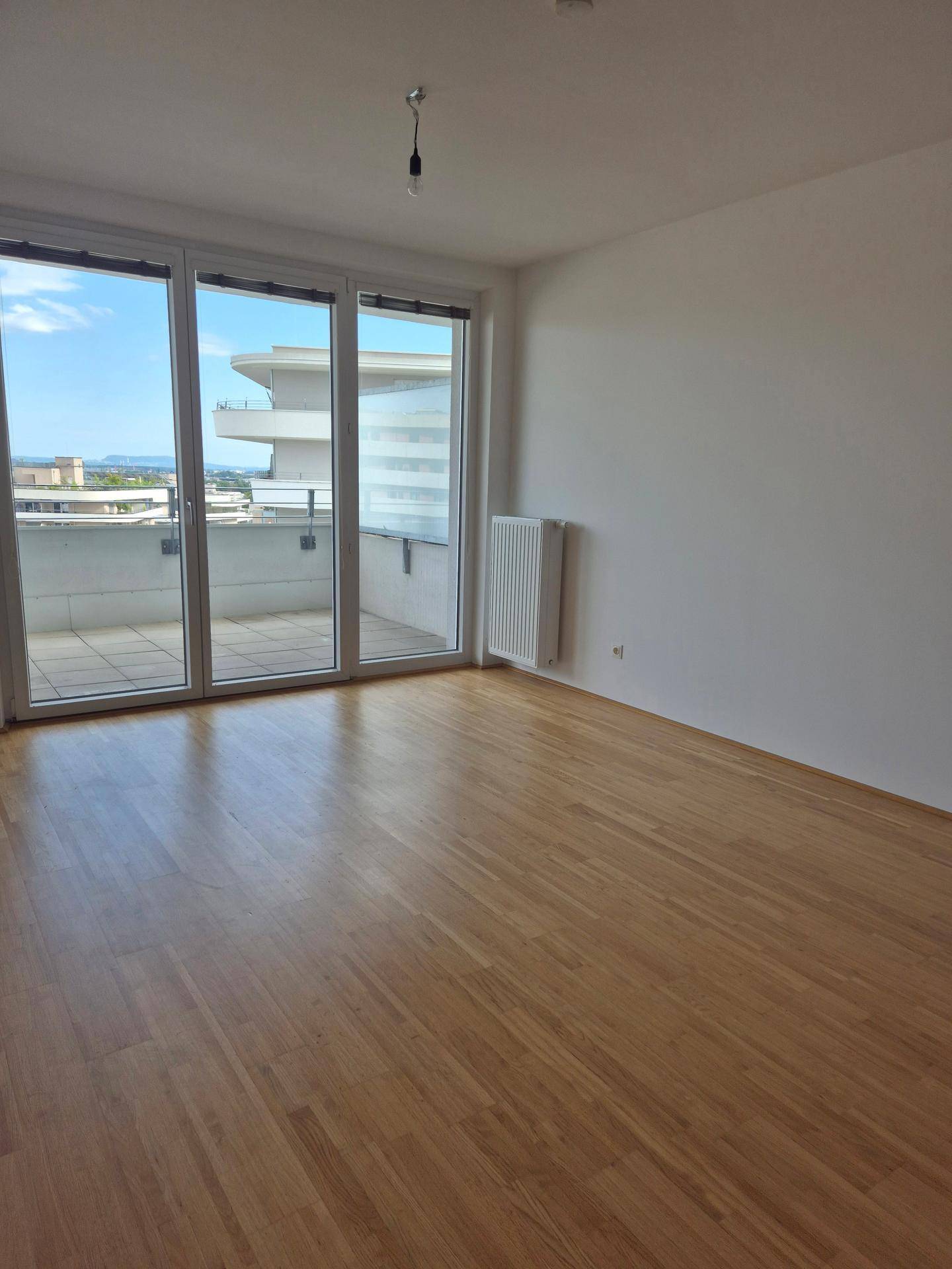 Heller Wohnraum mit Holzboden und großen Fenstern, die Zugang zu einem Balkon oder einer Terrasse bieten.
