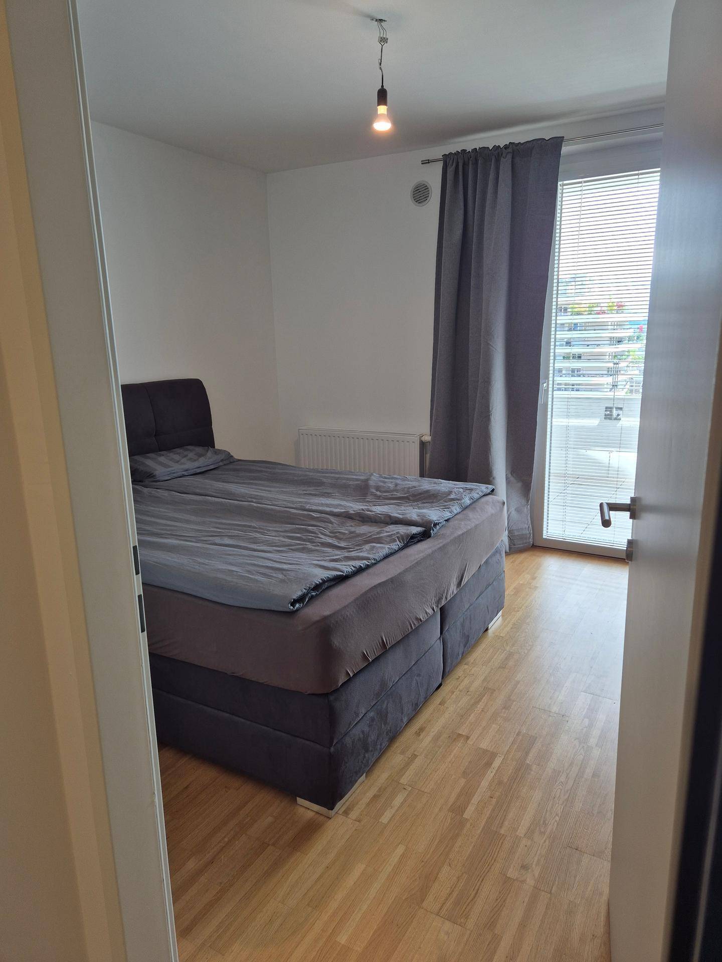 Gemütliches Schlafzimmer mit Doppelbett und hellem Laminatboden, bietet direkten Zugang zu einem Balkon.