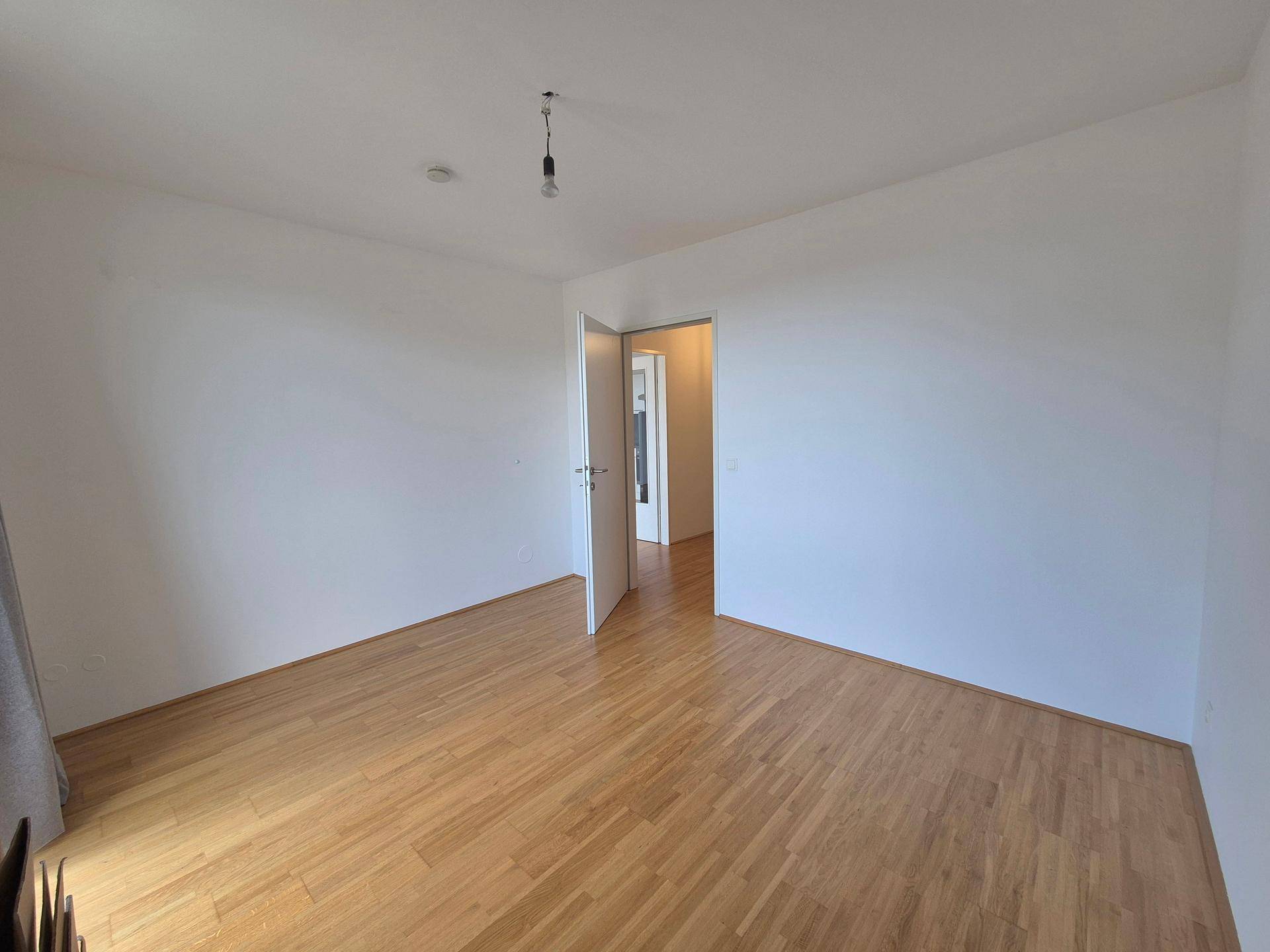 Geräumiges Schlafzimmer mit hellem Holzboden und weißen Wänden, bereit zur individuellen Gestaltung.