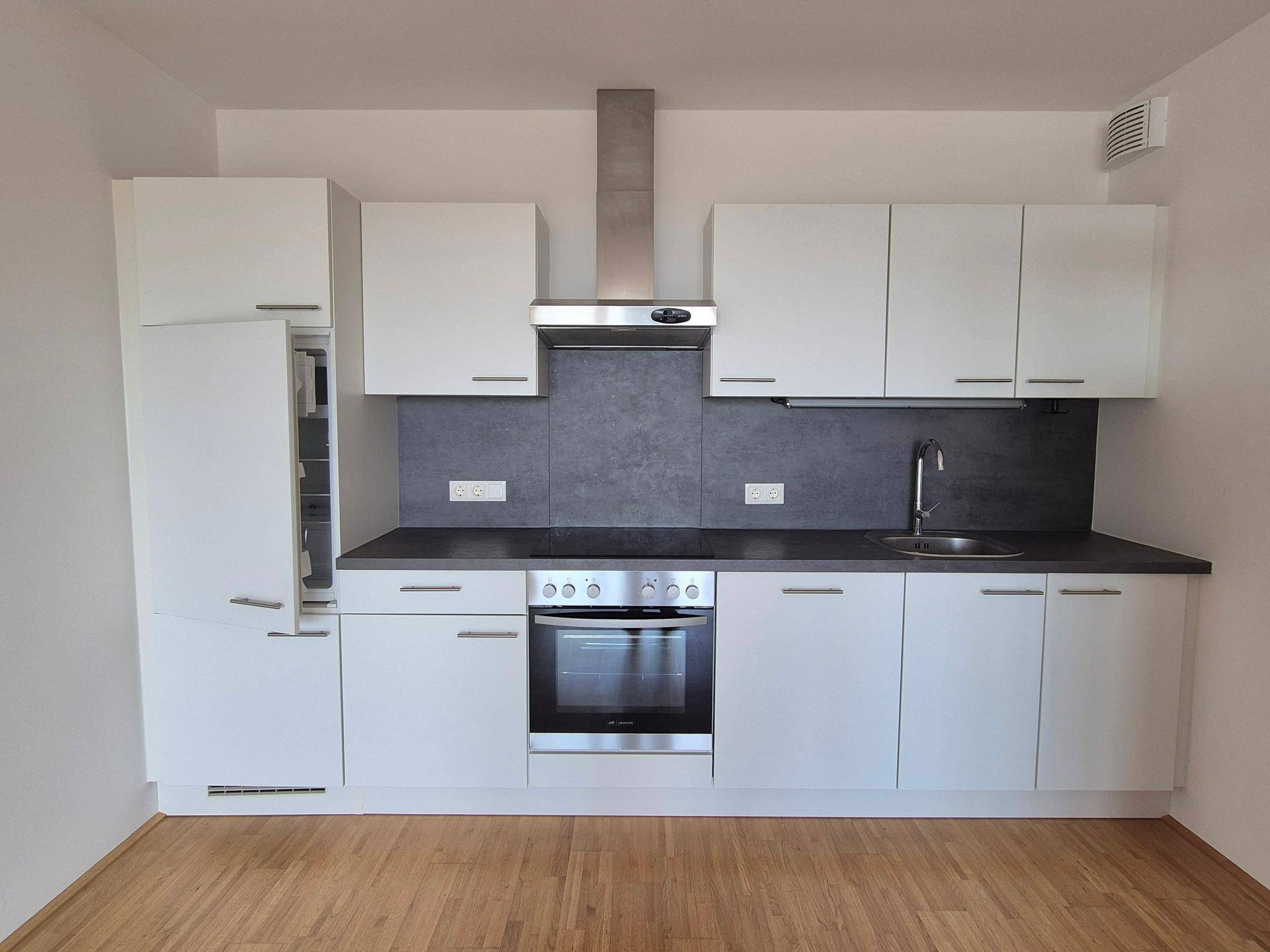 Moderne Einbauküche mit weißen Schränken, dunkler Arbeitsplatte und integrierten Elektrogeräten.