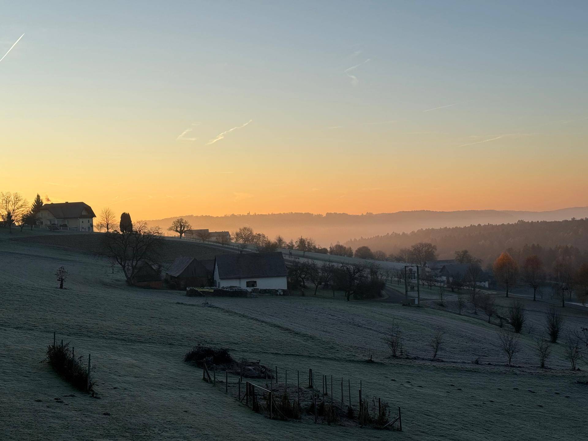 Morgendliche Landschaft mit Nebel über den Feldern und Häusern in der Ferne.