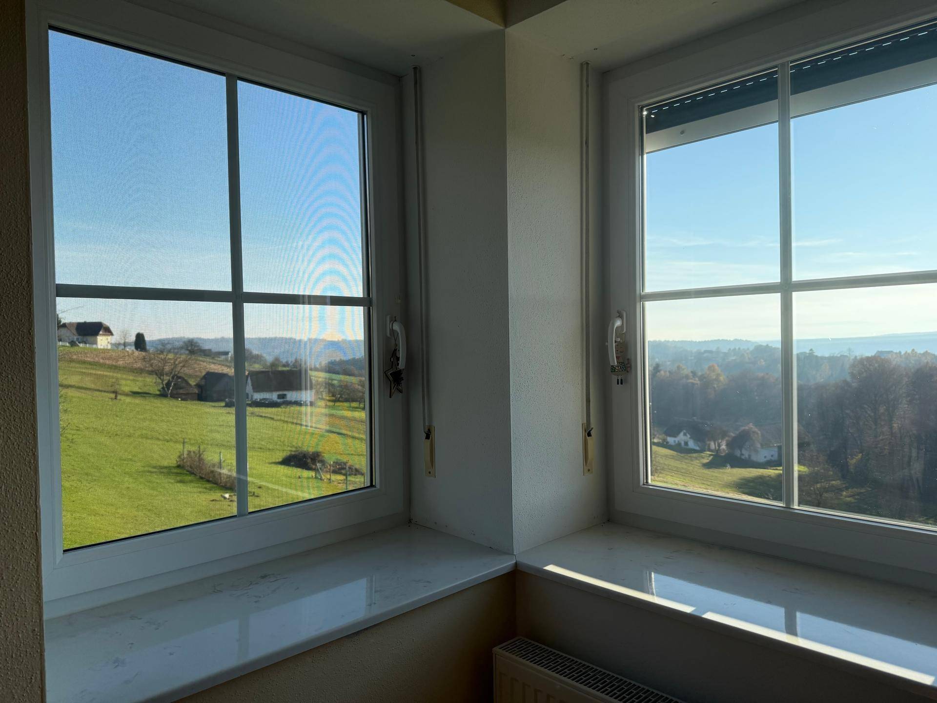 Helles Zimmer mit Eckfenstern, die einen weiten Blick auf die grüne Landschaft ermöglichen.