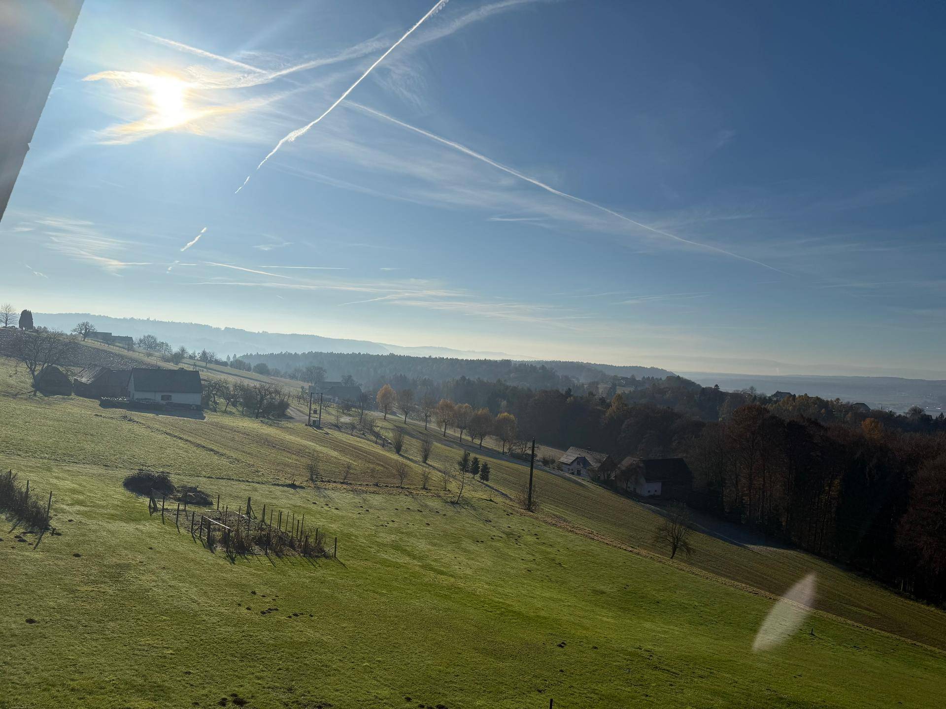 Sonnige Landschaft mit grünen Feldern, vereinzelten Häusern und weitem Himmel.