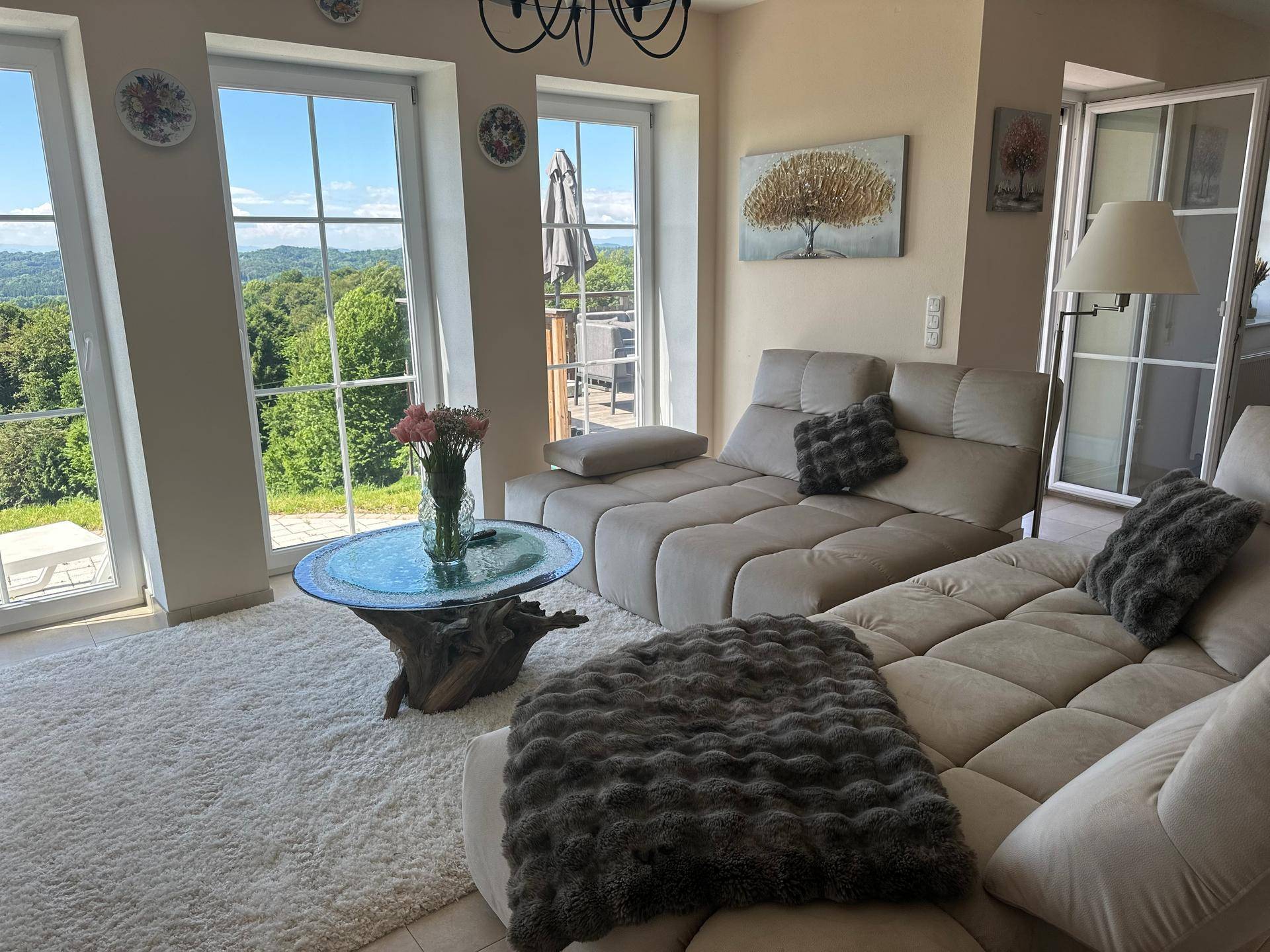 Gemütliches Wohnzimmer mit großem Sofa, hellem Teppich und Zugang zur Terrasse mit Weitblick.