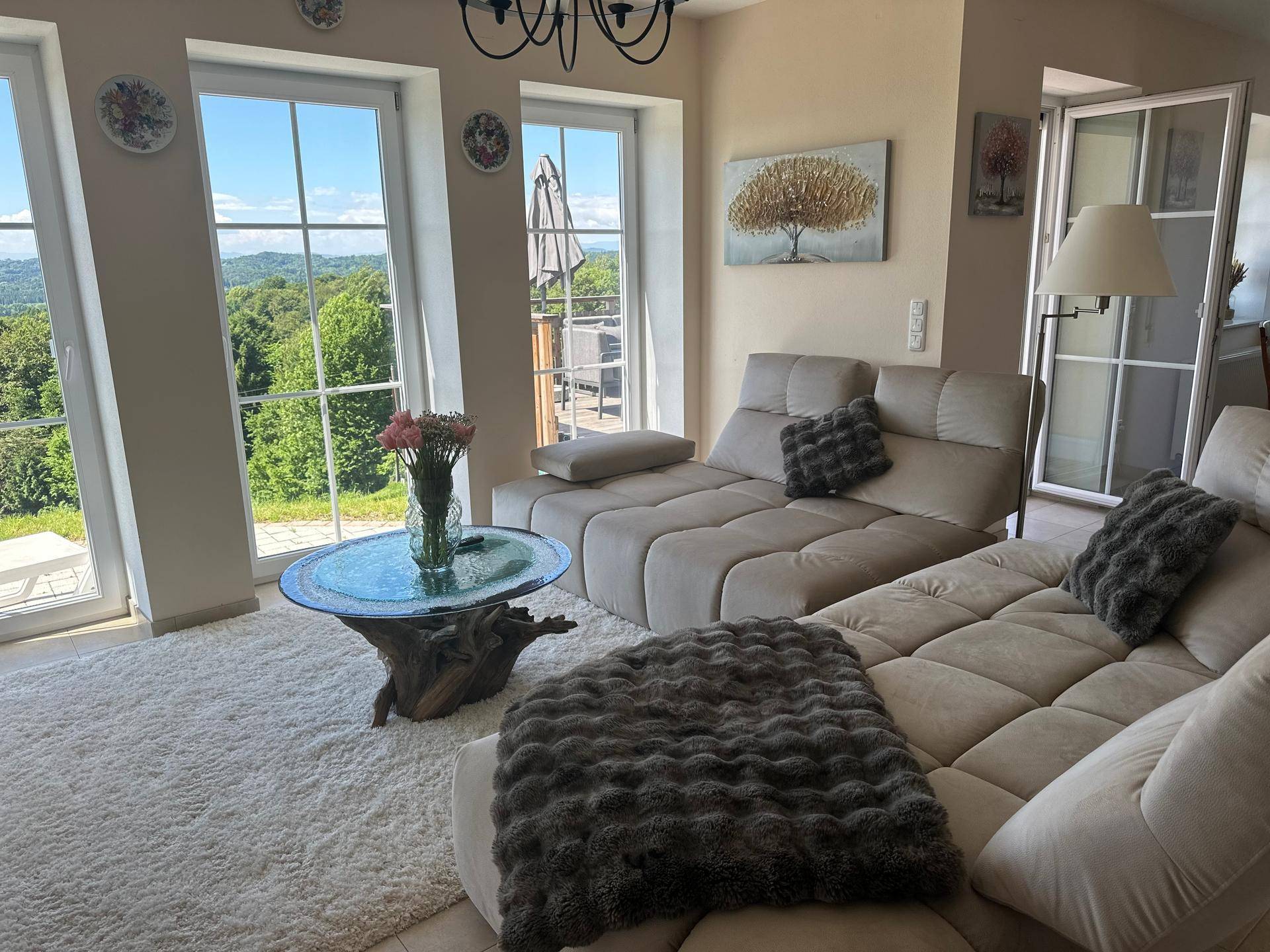 Helles Wohnzimmer mit beigem Sofa, Fliesenboden und weitem Blick ins Grüne.