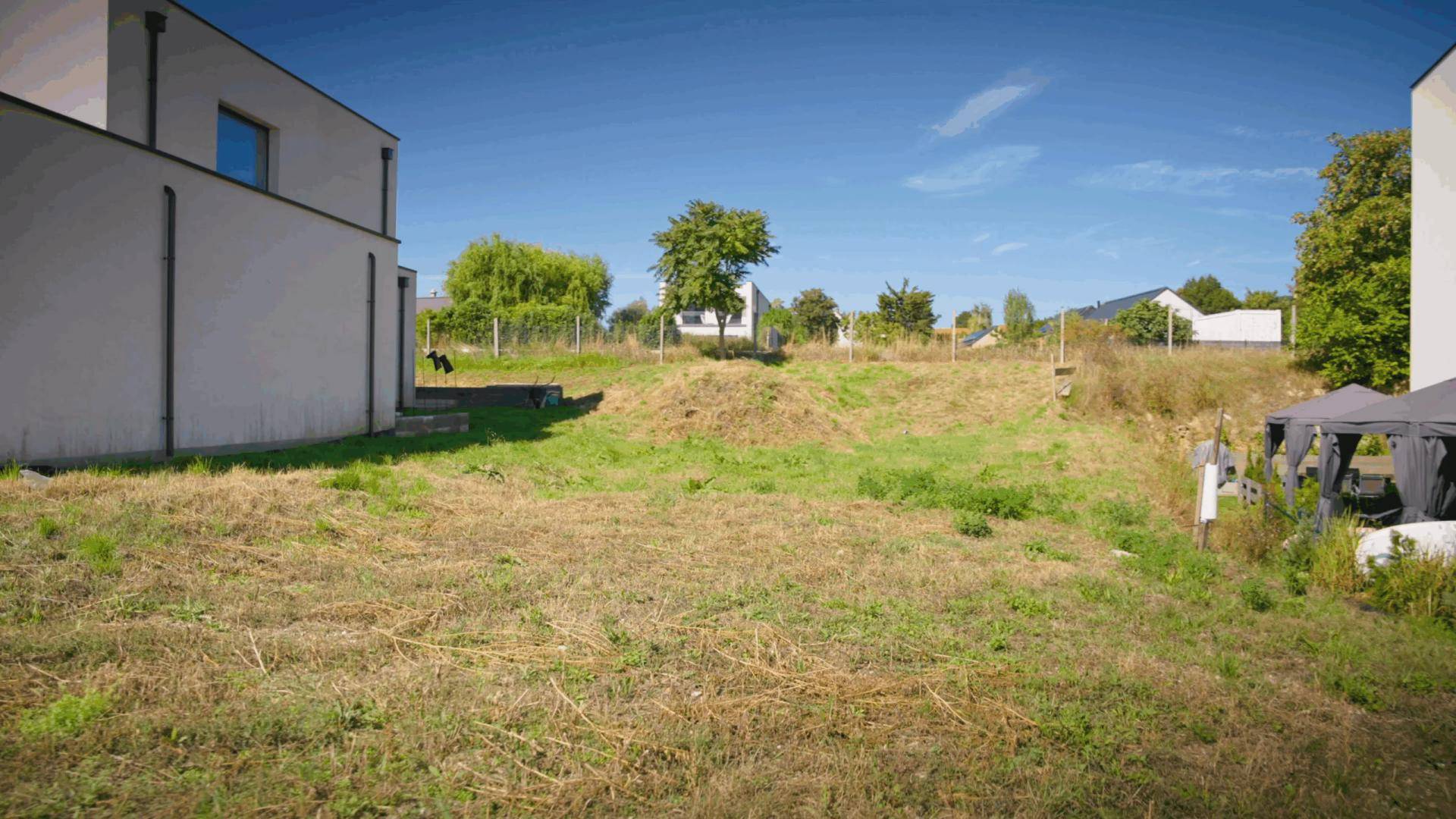 Unbebautes Grundstück mit trockener Grasfläche neben einem modernen Gebäude unter klarem blauem Himmel.