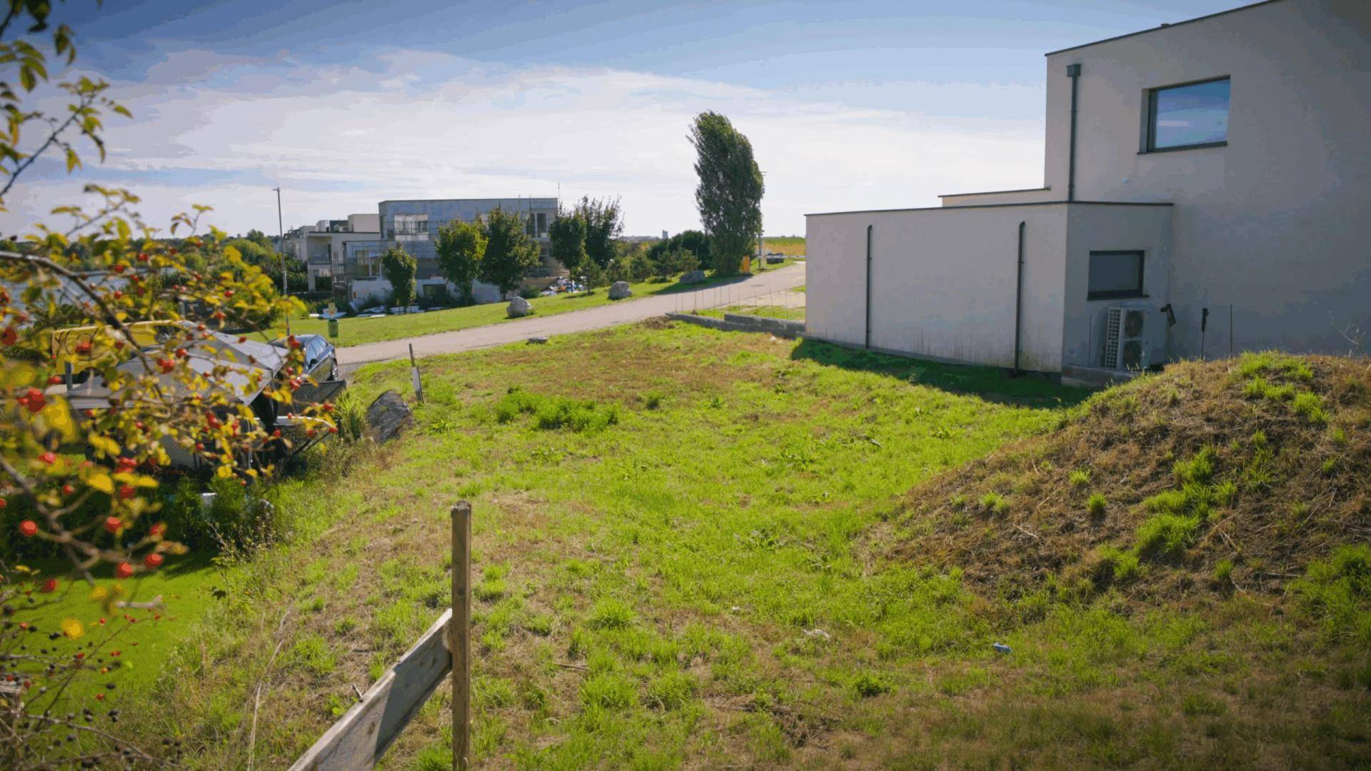 Unbebautes Grundstück mit Grasfläche neben einem modernen Gebäude unter blauem Himmel.