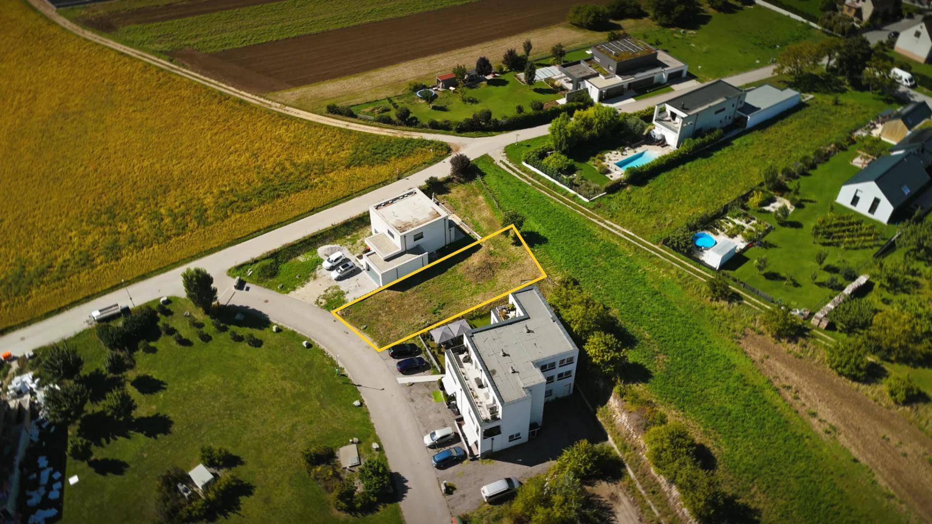 Luftaufnahme von Wohnhäusern mit einem markierten Grundstück, umgeben von Feldern und Straßen.