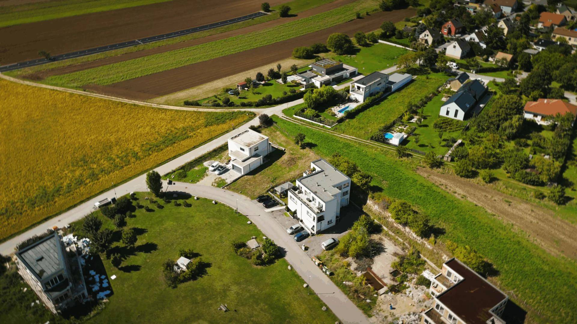 Luftaufnahme von Wohnhäusern und unbebauten Grundstücken, umgeben von Feldern und Grünflächen.