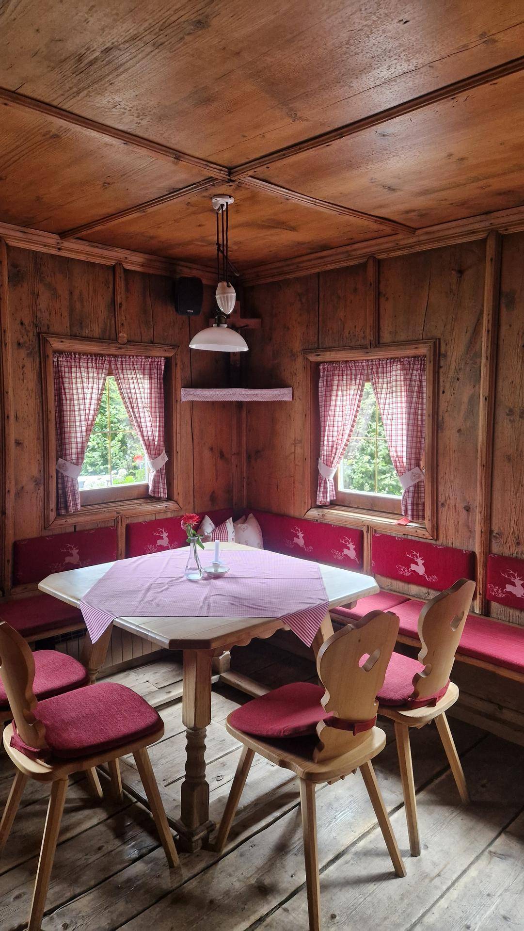 Gemütlicher Essbereich in einem traditionellen Wirtshaus mit Holztäfelung, roten Sitzbänken und karierten Vorhängen.