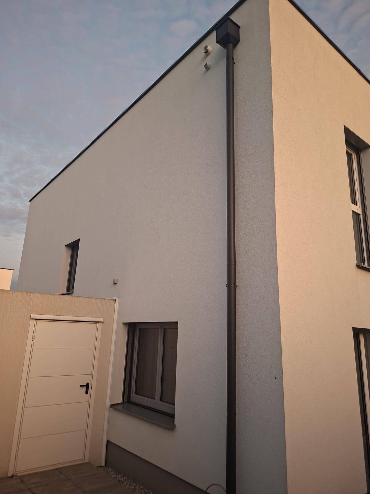 Seitenansicht des modernen Hauses mit Nebeneingangstür und Regenfallrohr.
