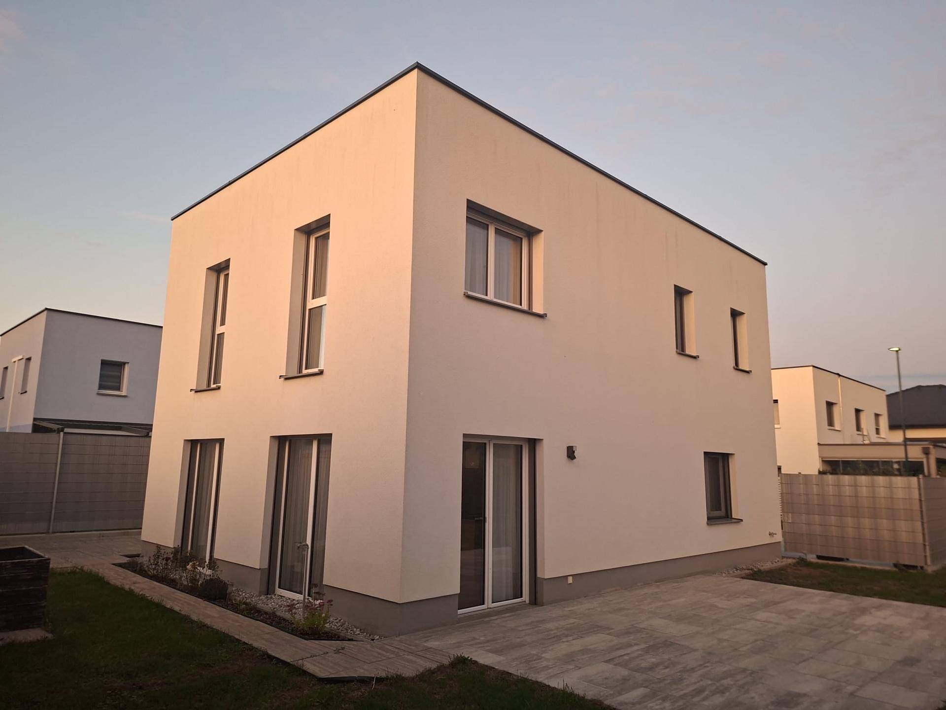 Modernes Einfamilienhaus mit weißer Fassade, Flachdach und gepflastertem Zugangsbereich.