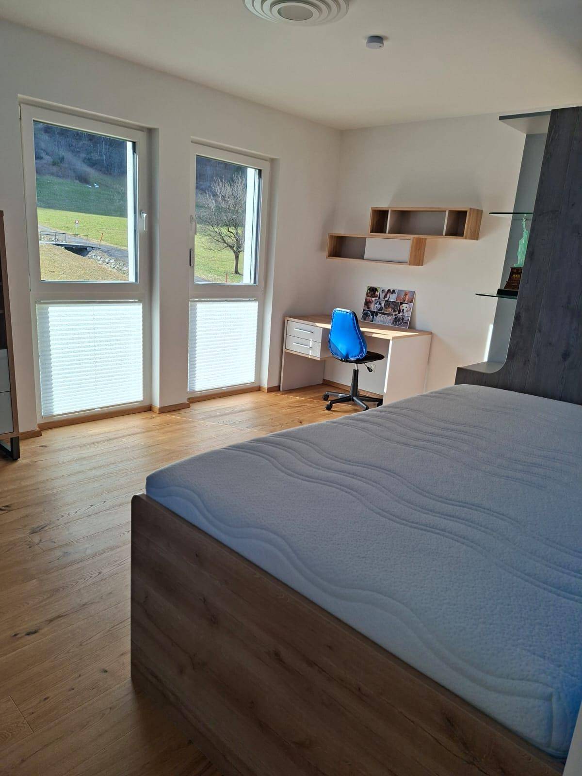 Lichtdurchflutetes Schlafzimmer mit Schreibtisch, Holzboden und weitem Blick in die Natur.