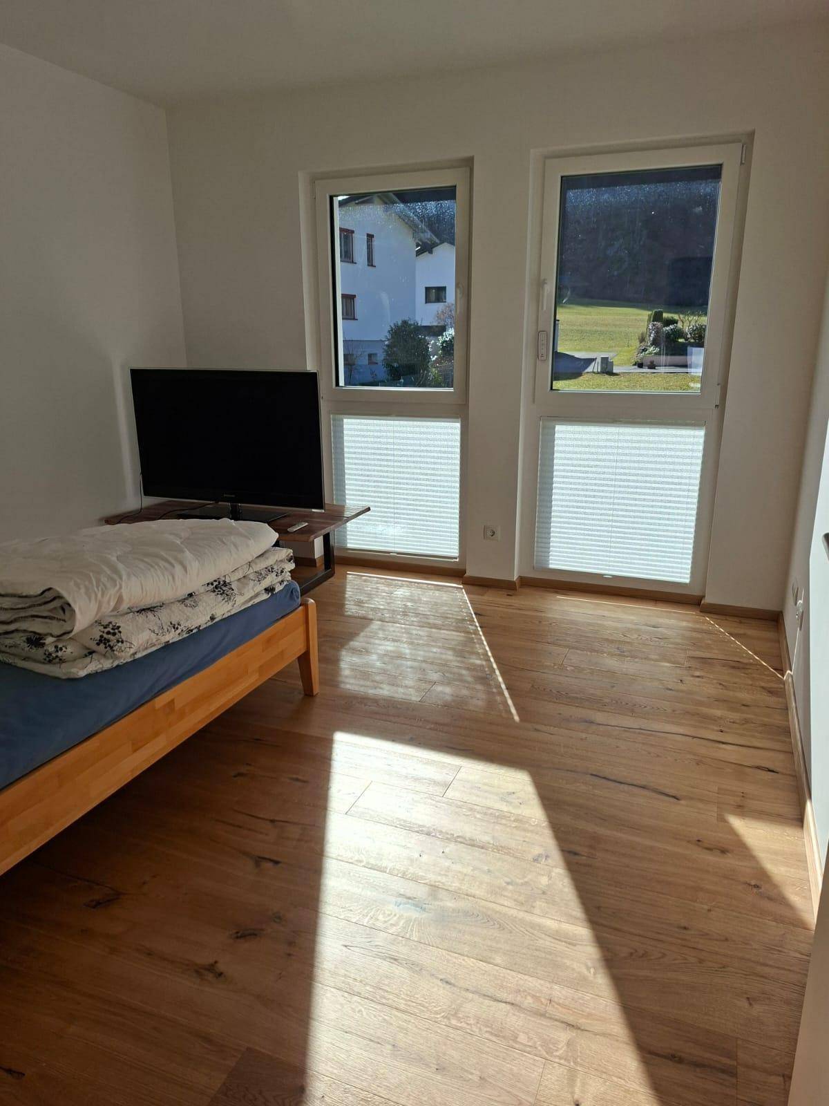 Helles Schlafzimmer mit Holzbett, Parkettboden und Blick ins Grüne.