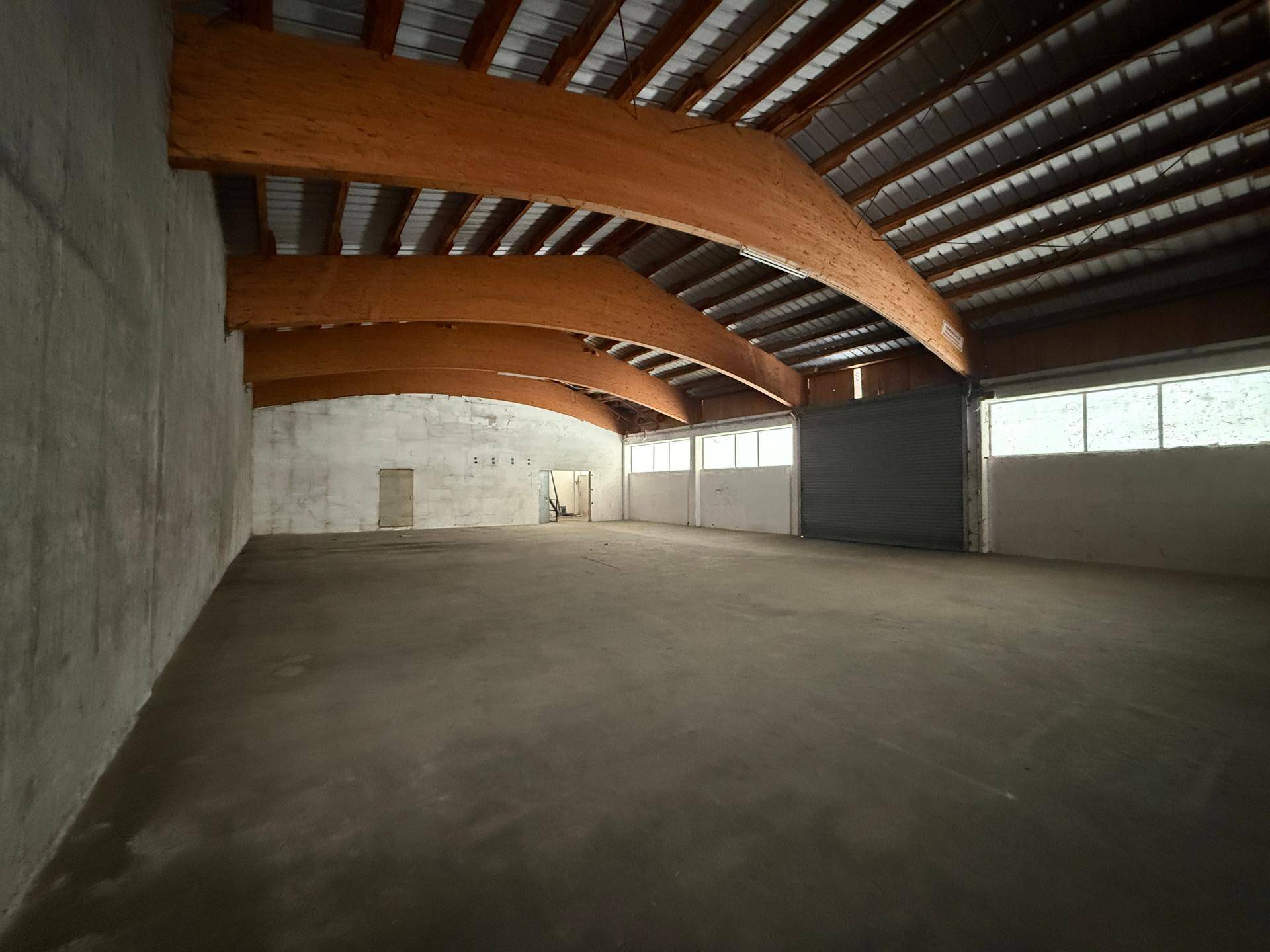 Große, leere Lagerhalle mit hohen Decken, sichtbaren Holzbalken und Betonboden.