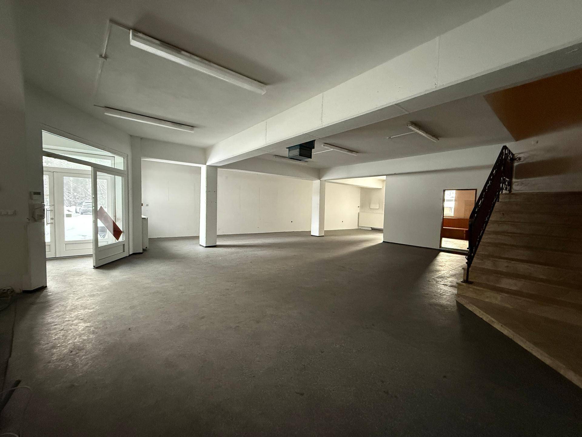 Heller, offener Gewerberaum mit Betonboden, weißen Wänden und einem Treppenaufgang, ideal für verschiedene Nutzungen.