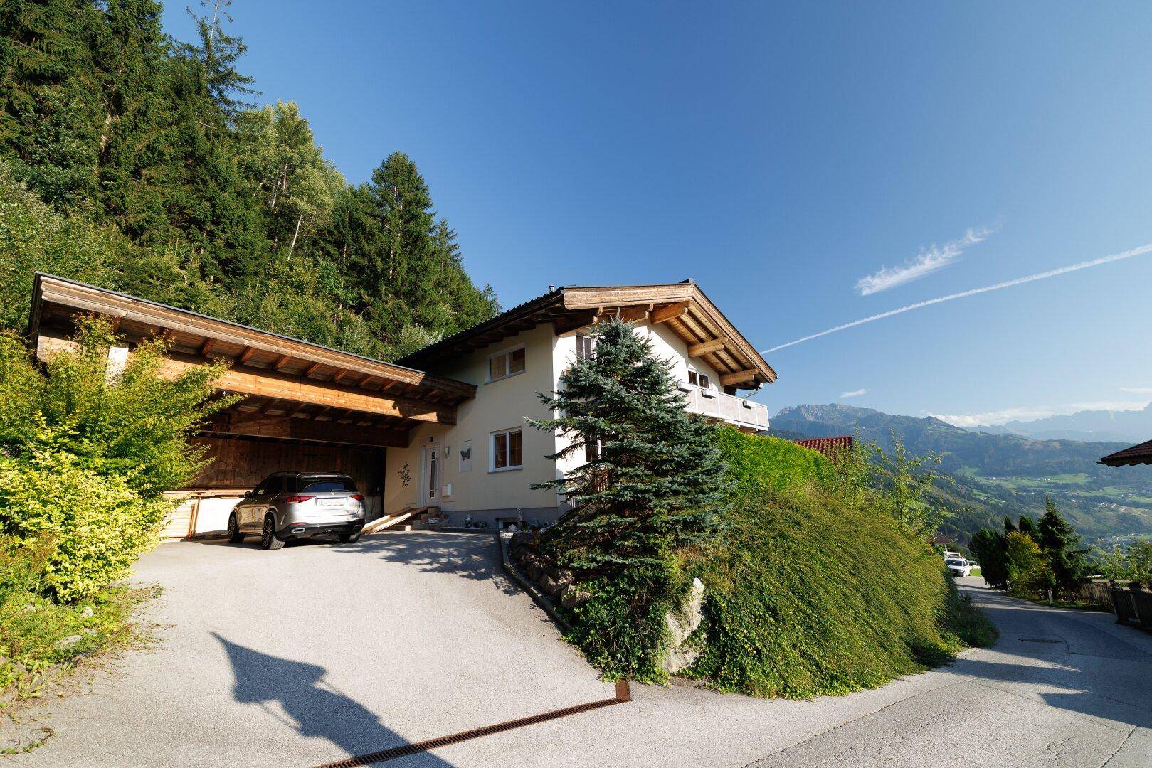 Traditionelles Haus mit Carport, umgeben von grüner Natur und mit Bergblick.
