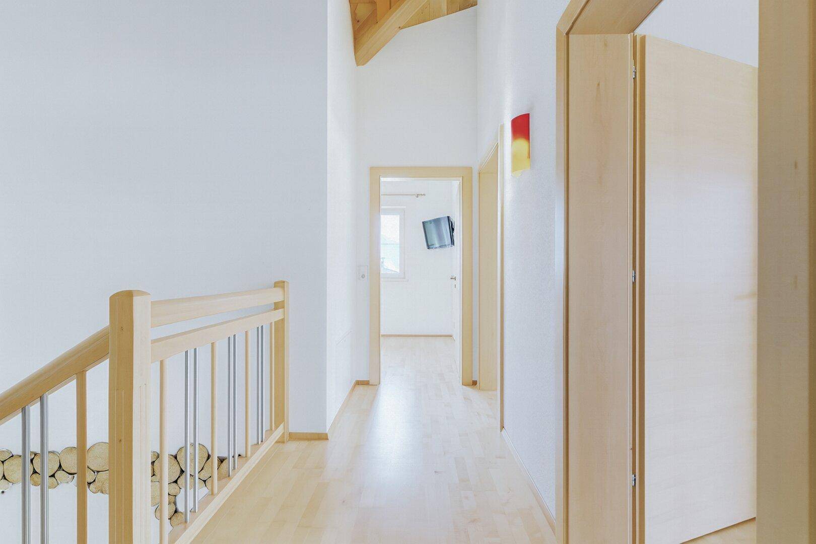 Heller Flur im Obergeschoss mit Holzgeländer, Parkettboden und Zugang zu weiteren Räumen.