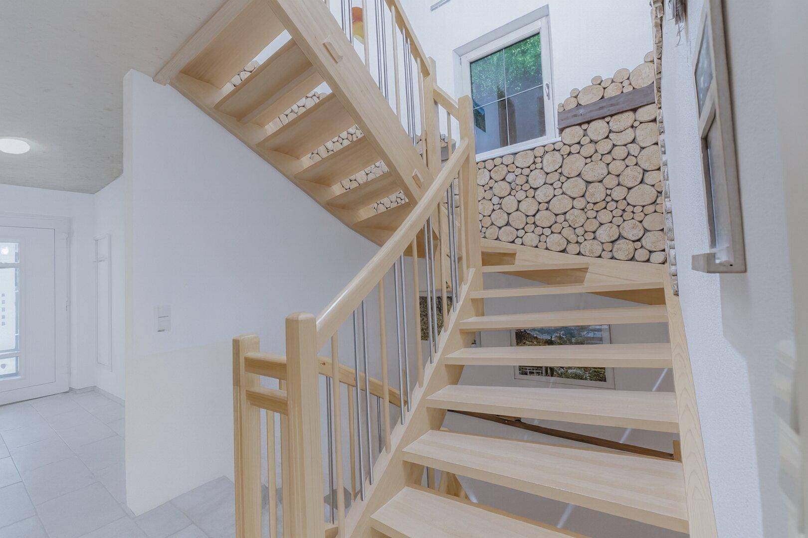 Holztreppe mit modernem Geländer und dekorativer Holzwand im Eingangsbereich.