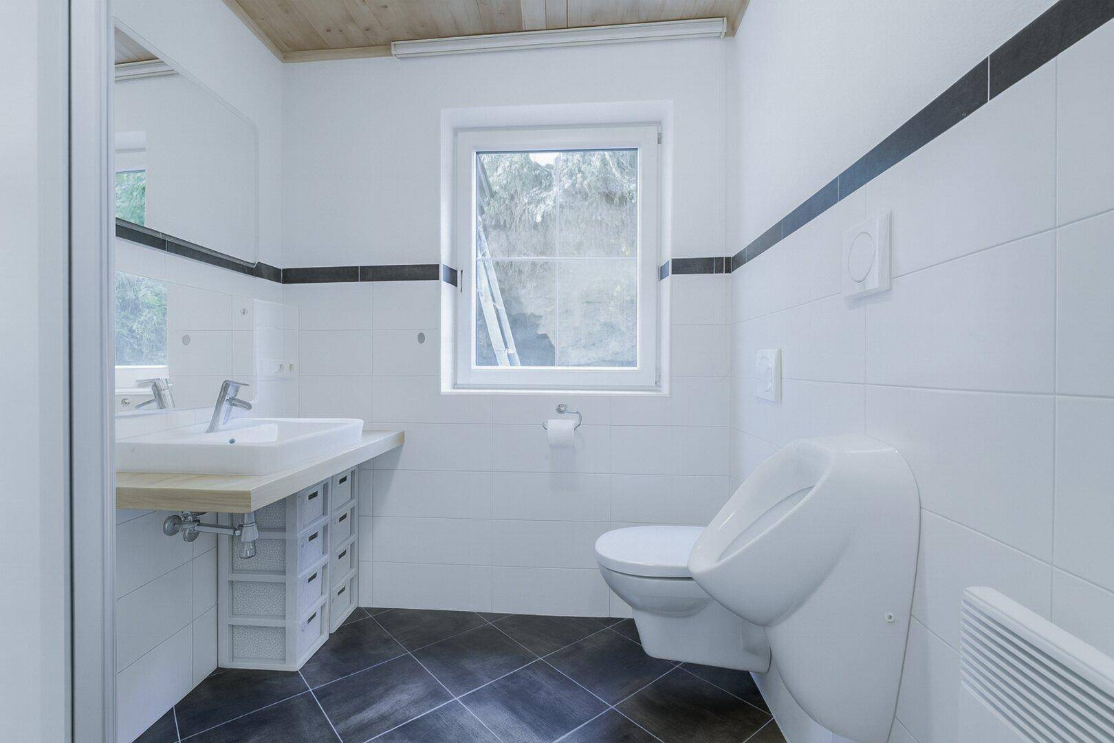 Modernes Gäste-WC mit Urinal, Waschbecken und dunklen Bodenfliesen.