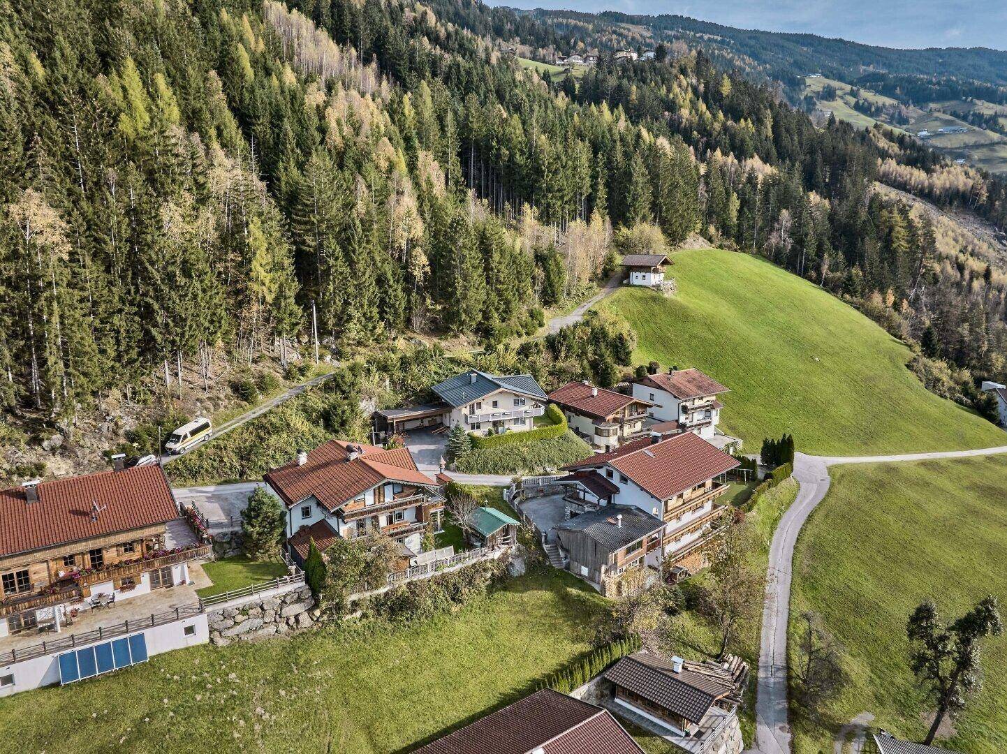 Luftaufnahme einer Siedlung in einer grünen Berglandschaft mit vielen Bäumen.