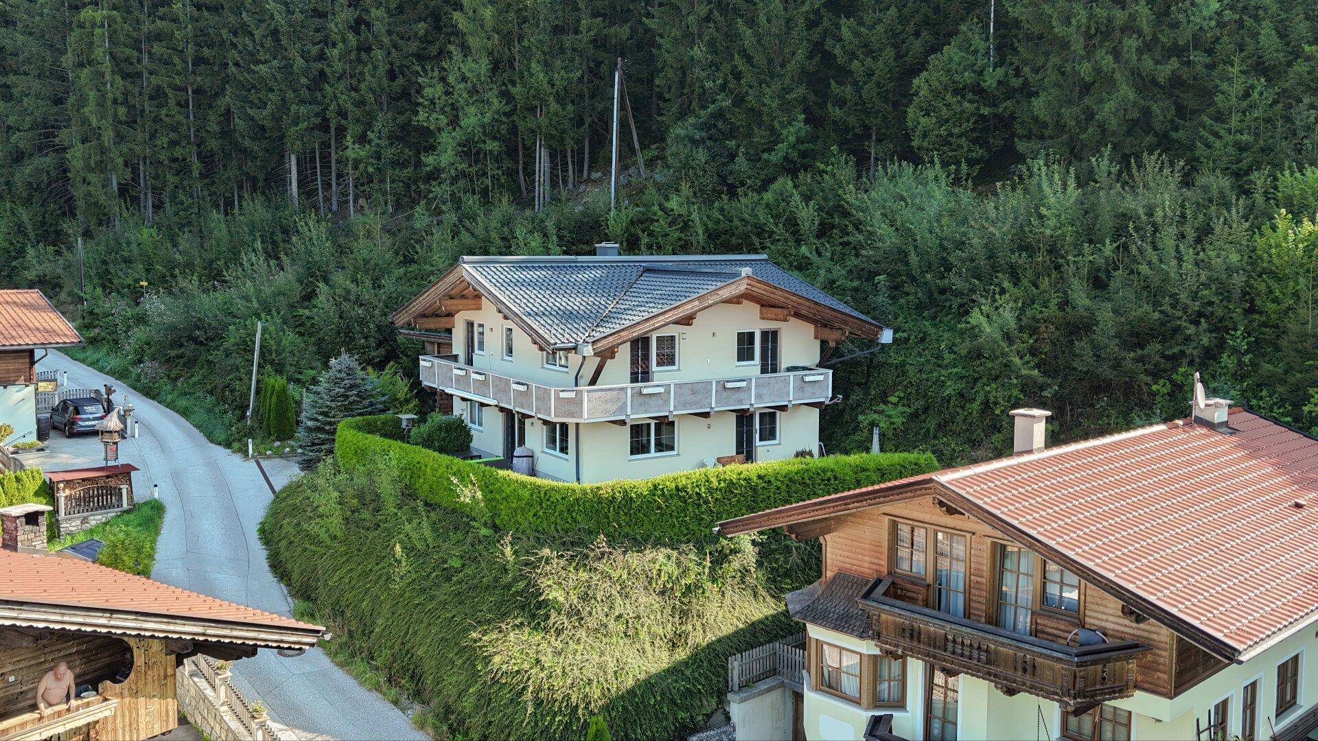Traditionelles Haus mit Balkonen und gepflegter Hecke, eingebettet in die Natur.