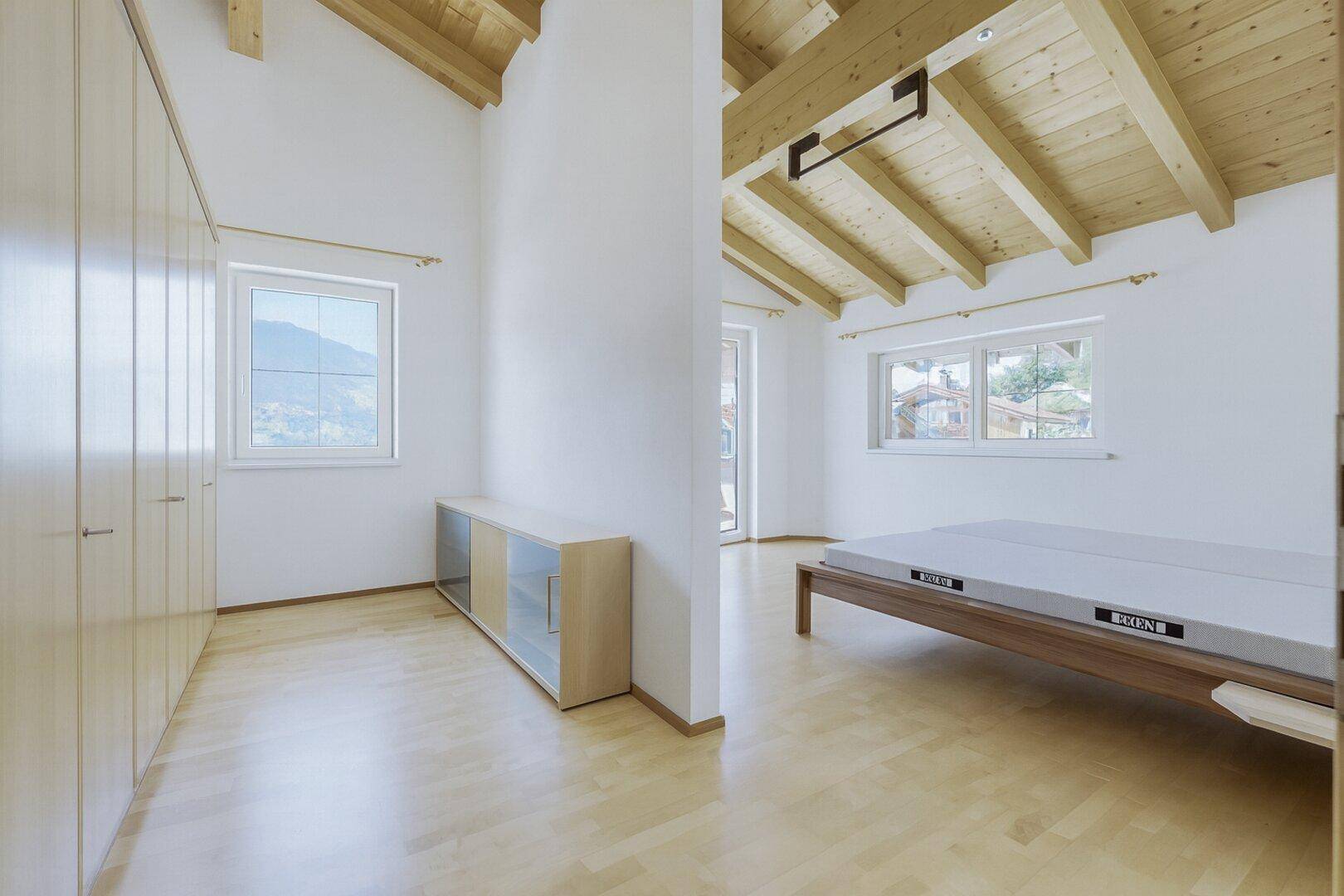 Geräumiges Schlafzimmer mit Holzbalkendecke, Parkettboden und Einbauschränken.