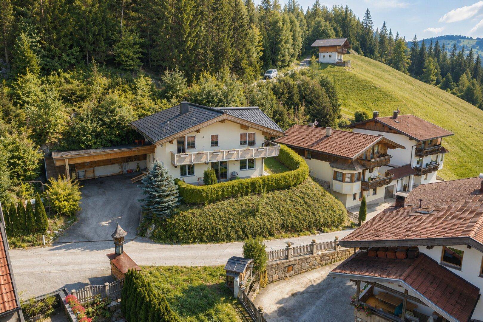 Luftaufnahme eines charmanten Chalets mit umliegenden Häusern in alpiner Berglandschaft.