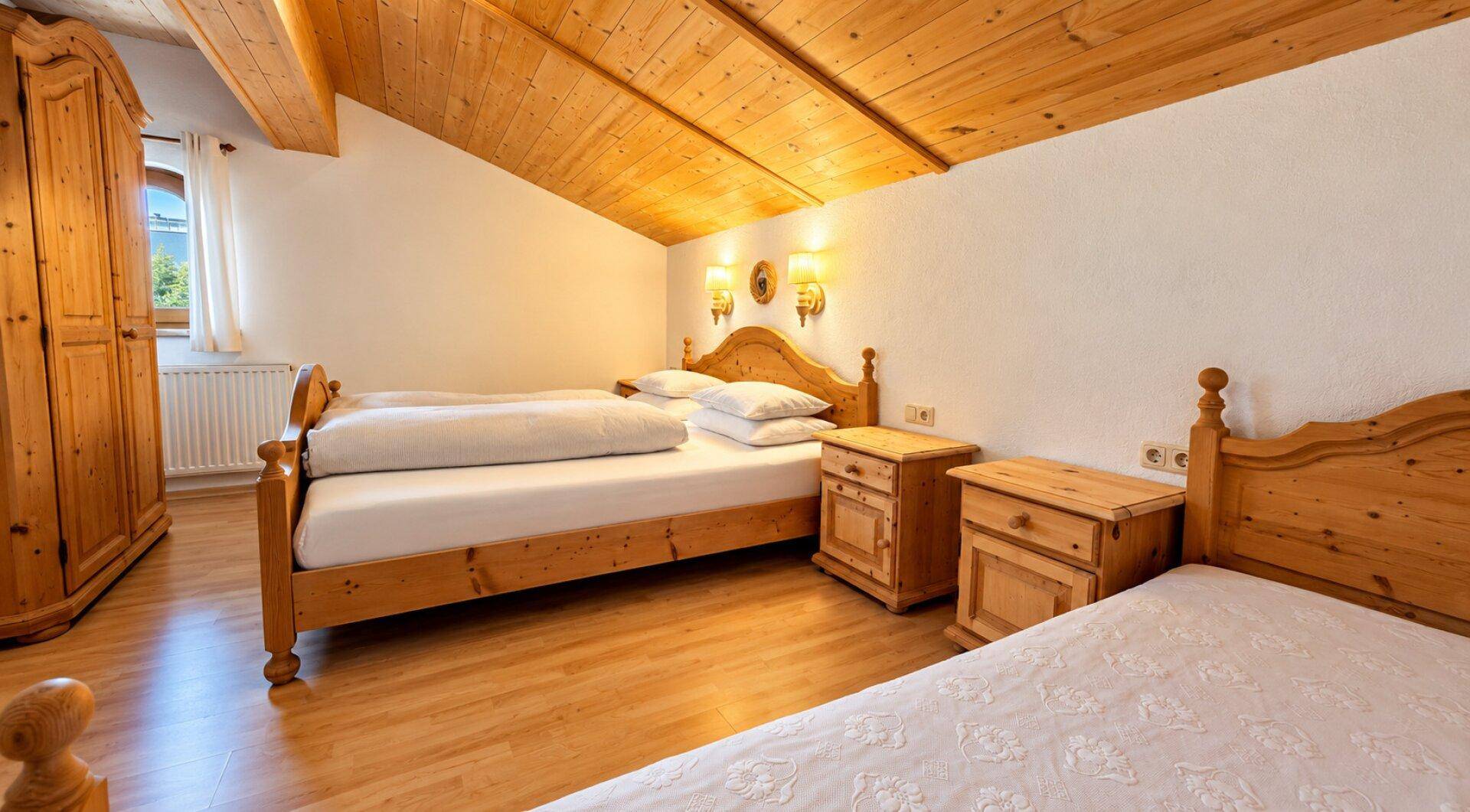 Schlafzimmer mit Holzbalkendecke, zwei Einzelbetten und Kleiderschrank im Dachgeschoss.