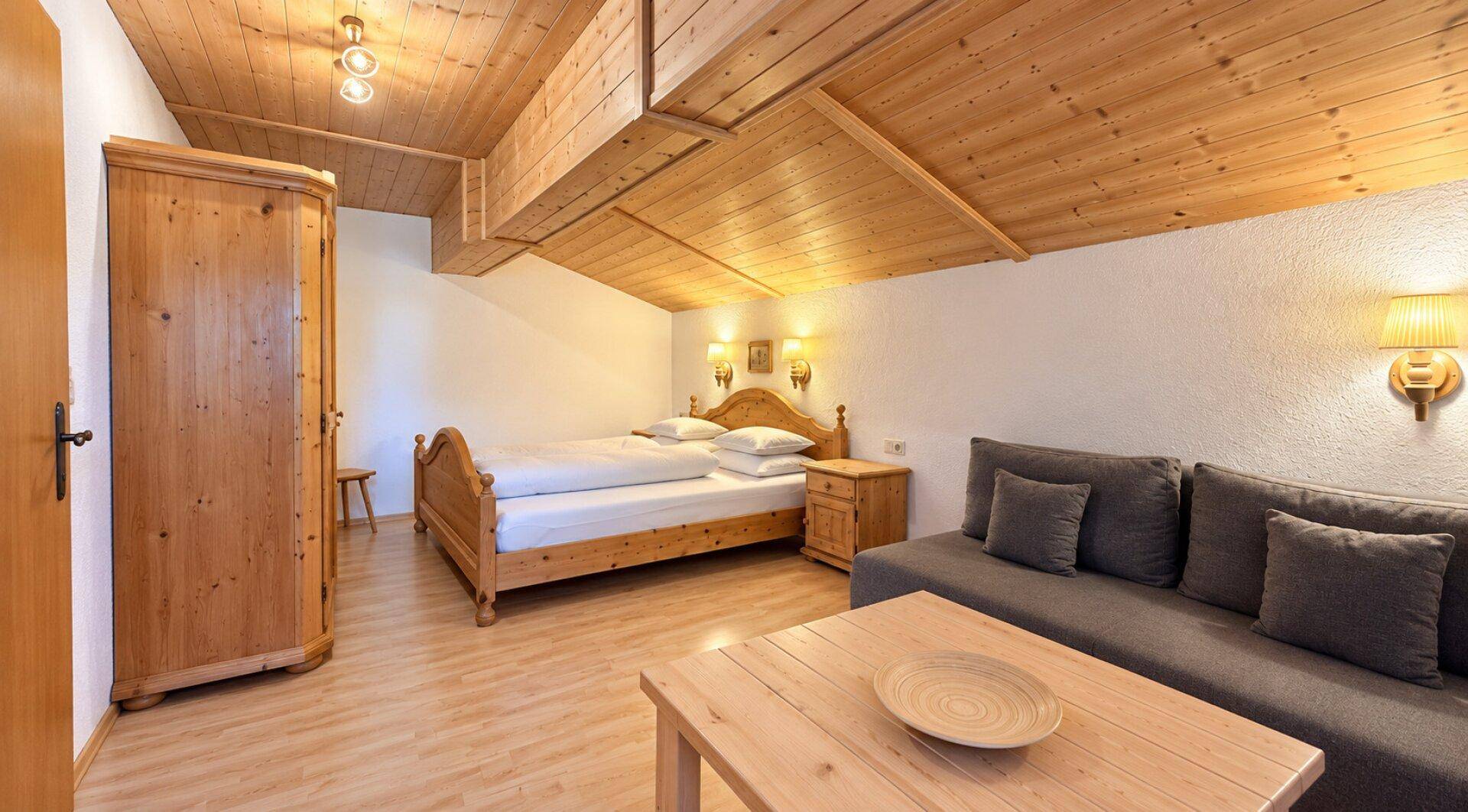 Geräumiges Schlafzimmer mit Holzbalkendecke, Doppelbett, Sofa und Kleiderschrank.