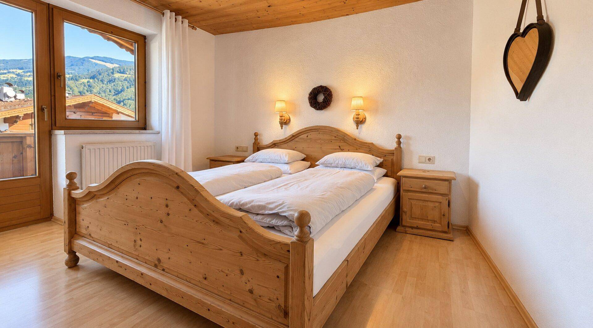 Gemütliches Schlafzimmer mit Holzdoppelbett, Holzbalkendecke und Bergblick vom Fenster.