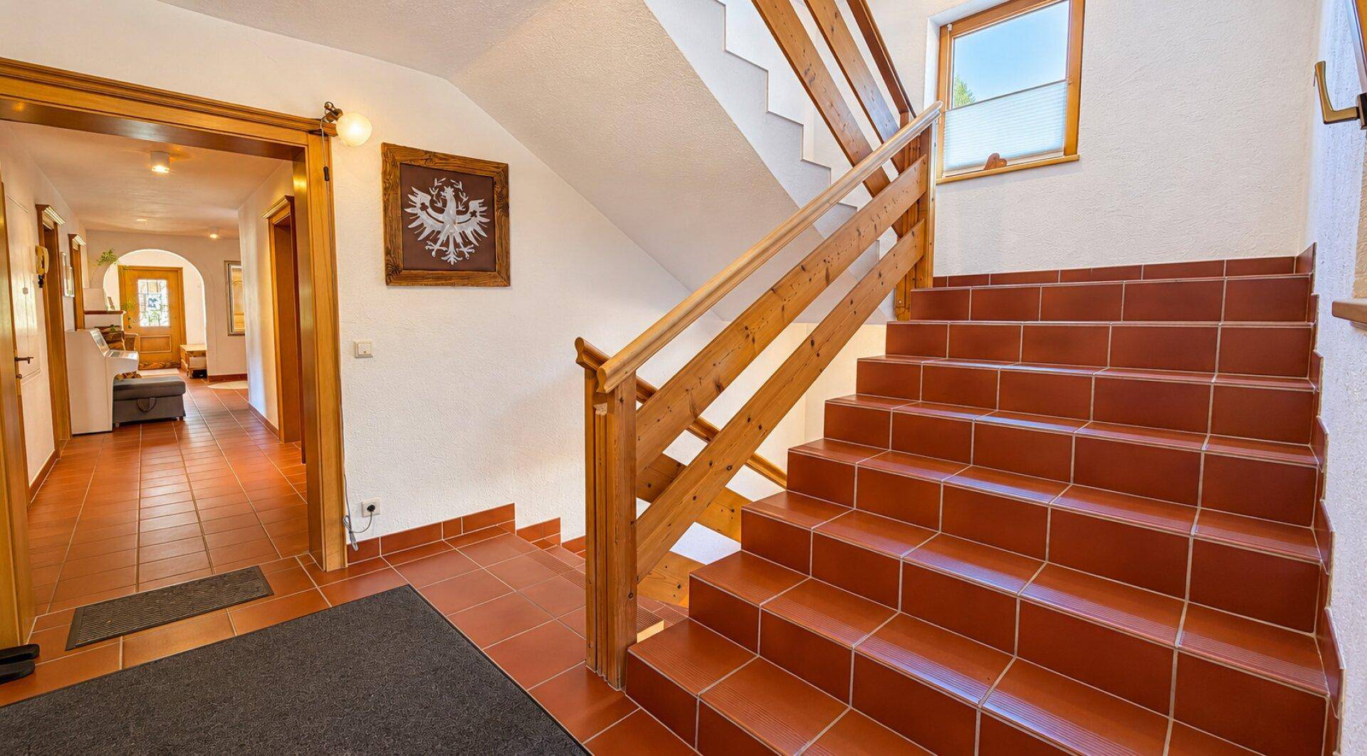 Heller Eingangsbereich mit Holztreppe, Terrakottafliesen und traditioneller Wanddekoration.