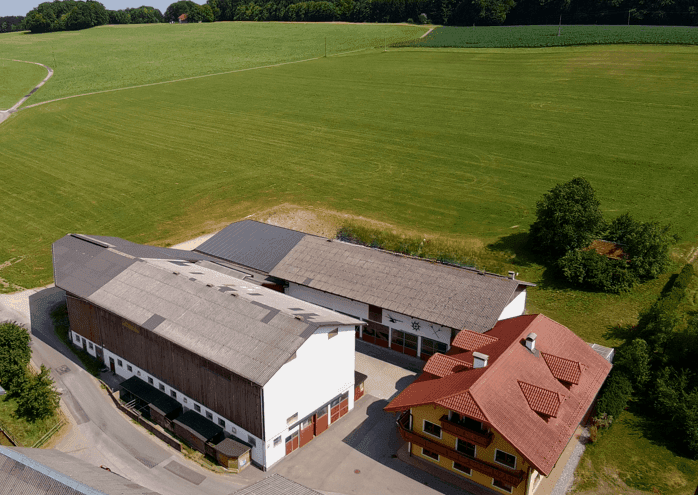 Luftaufnahme eines Anwesens mit Wohnhaus, Wirtschaftsgebäuden und umliegenden Feldern.