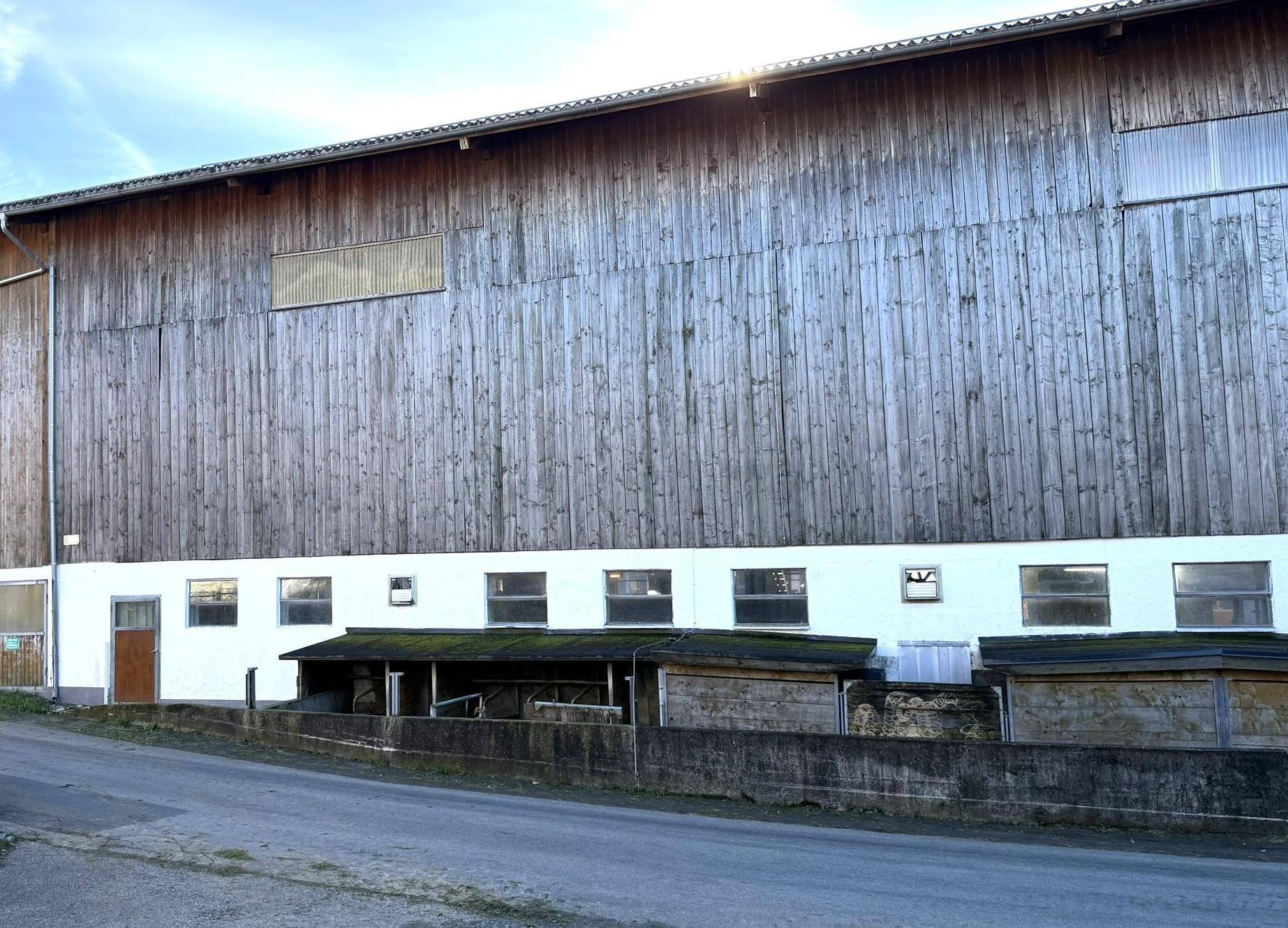 Große Holzfassade eines landwirtschaftlichen Gebäudes mit kleinen Fenstern und Zufahrt.