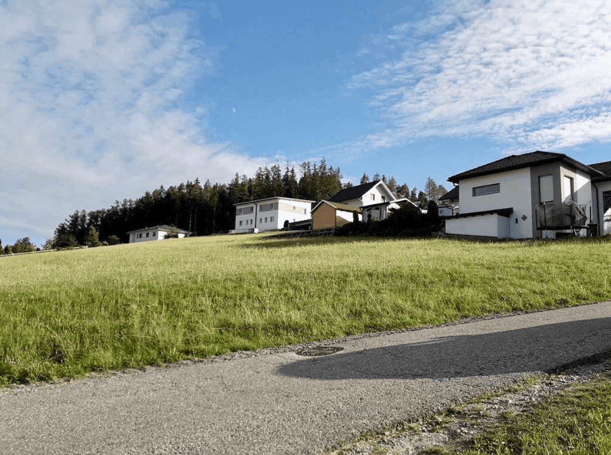 Idyllische ländliche Szene mit Wohnhäusern, einer weiten Wiese und einem Weg unter blauem Himmel.